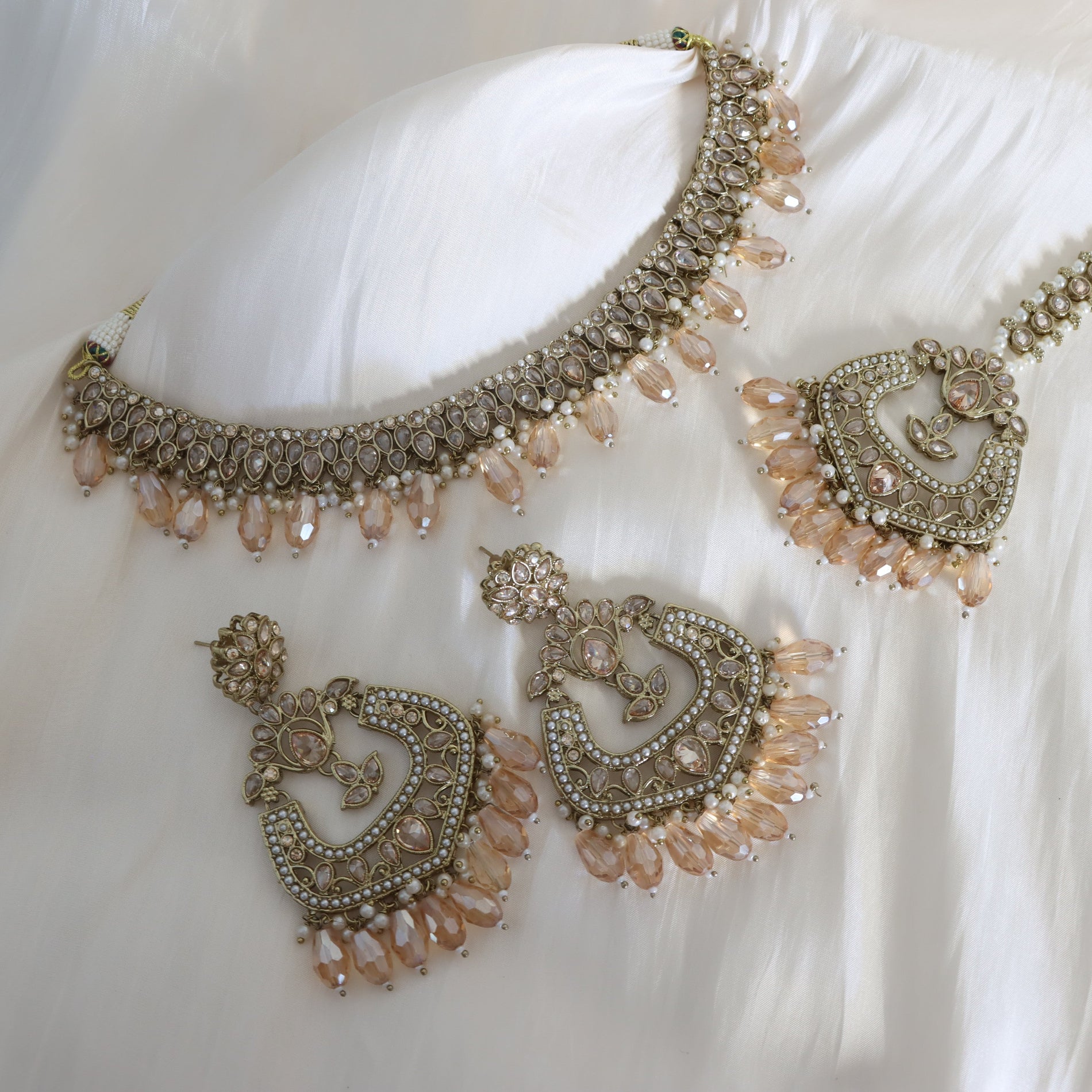 Ornate necklace and earrings set on a white fabric background