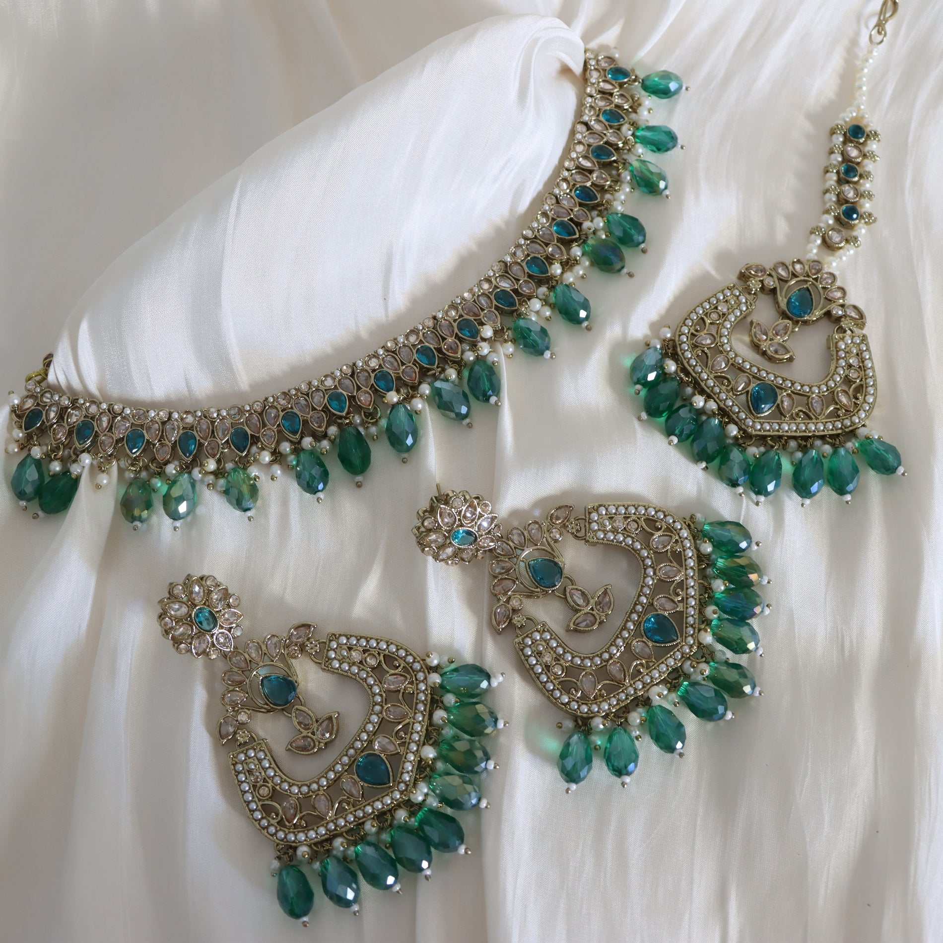Ornate necklace and earrings with green gemstones on a white fabric background