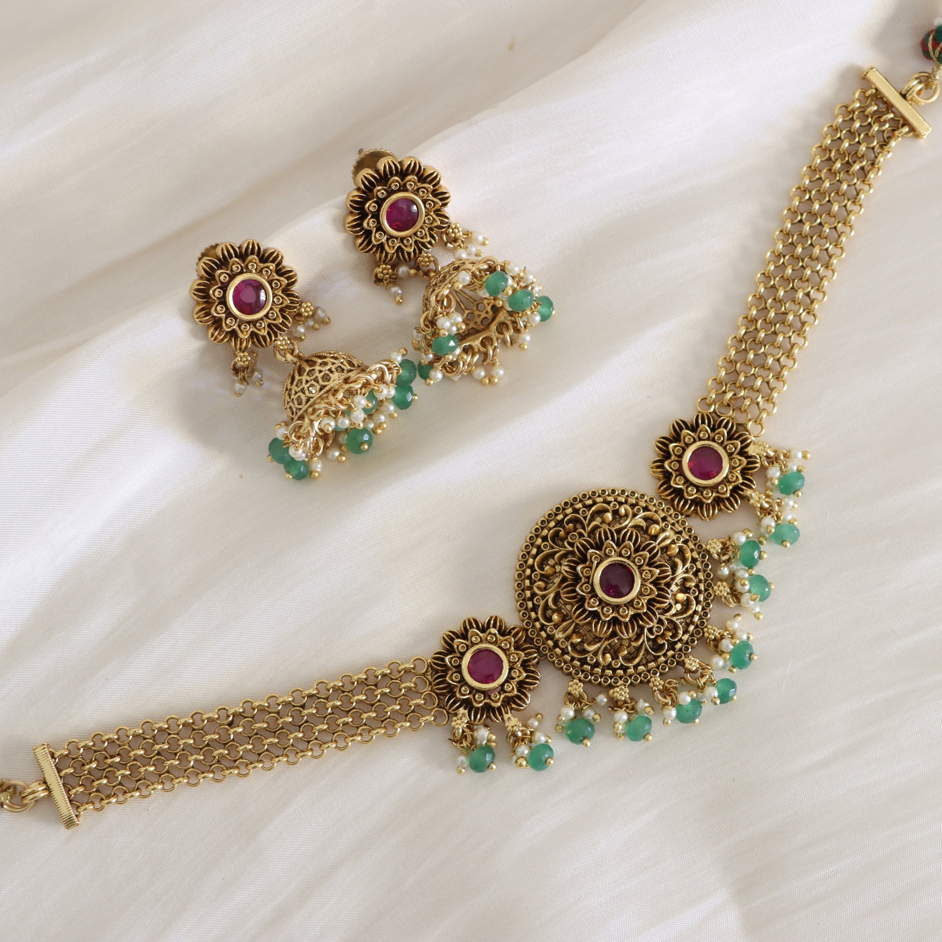 Gold necklace with red and green gemstones on a white fabric background