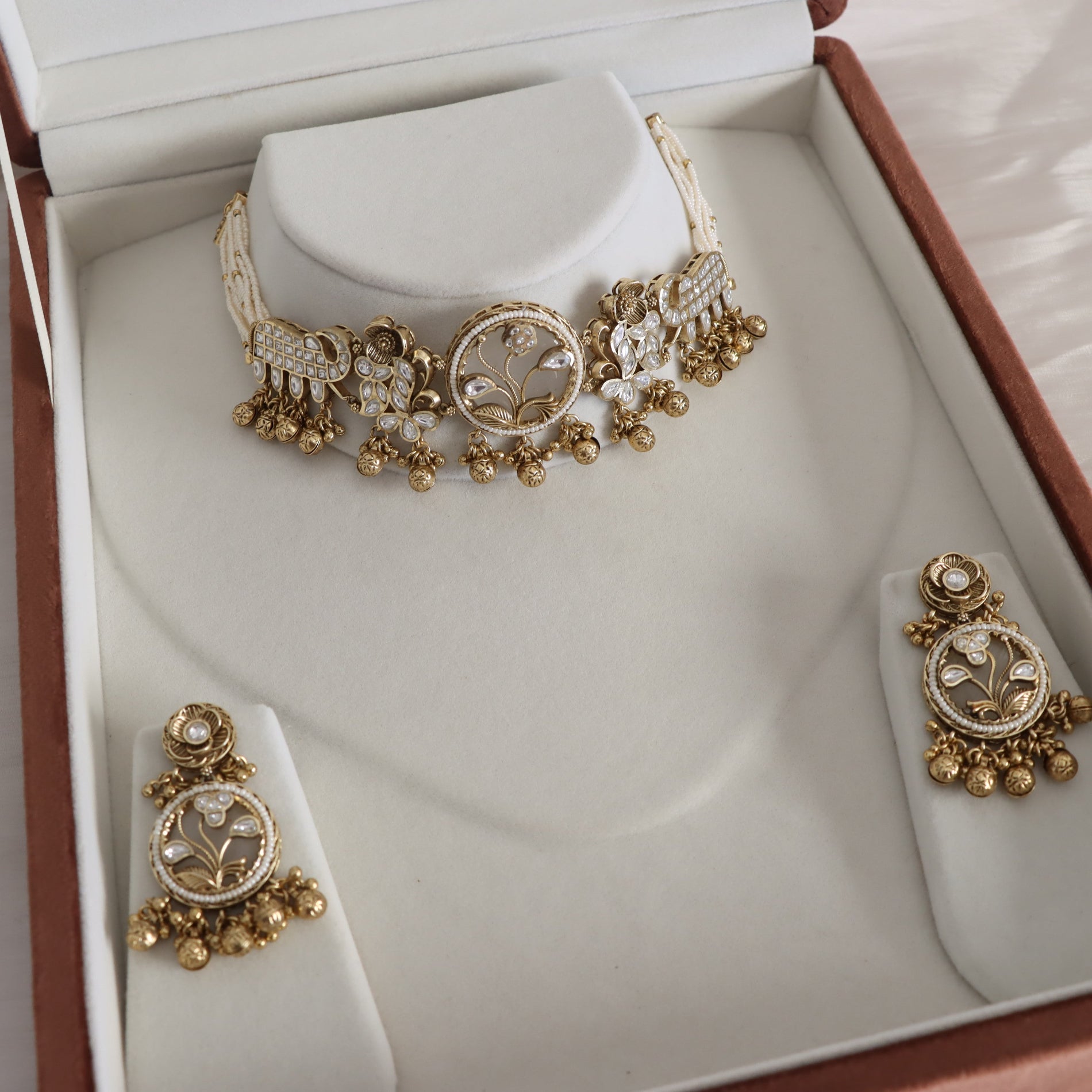Gold and white beaded jewelry set including a choker necklace, earrings, and a bracelet, displayed inside an open presentation box with cream-colored velvet inserts.