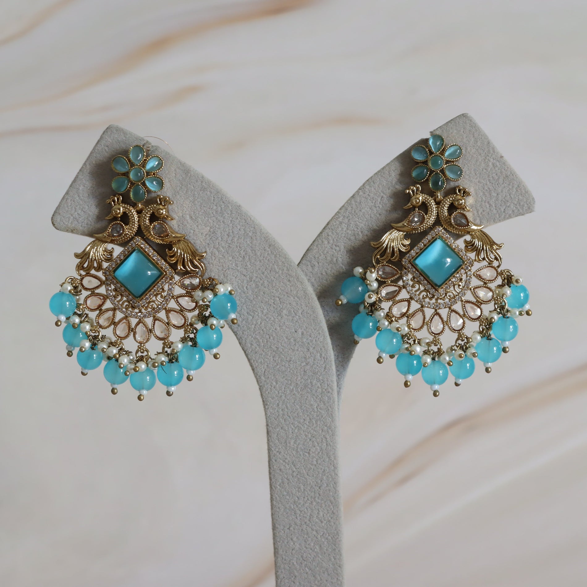Pair of ornate earrings with turquoise stones on a neutral background