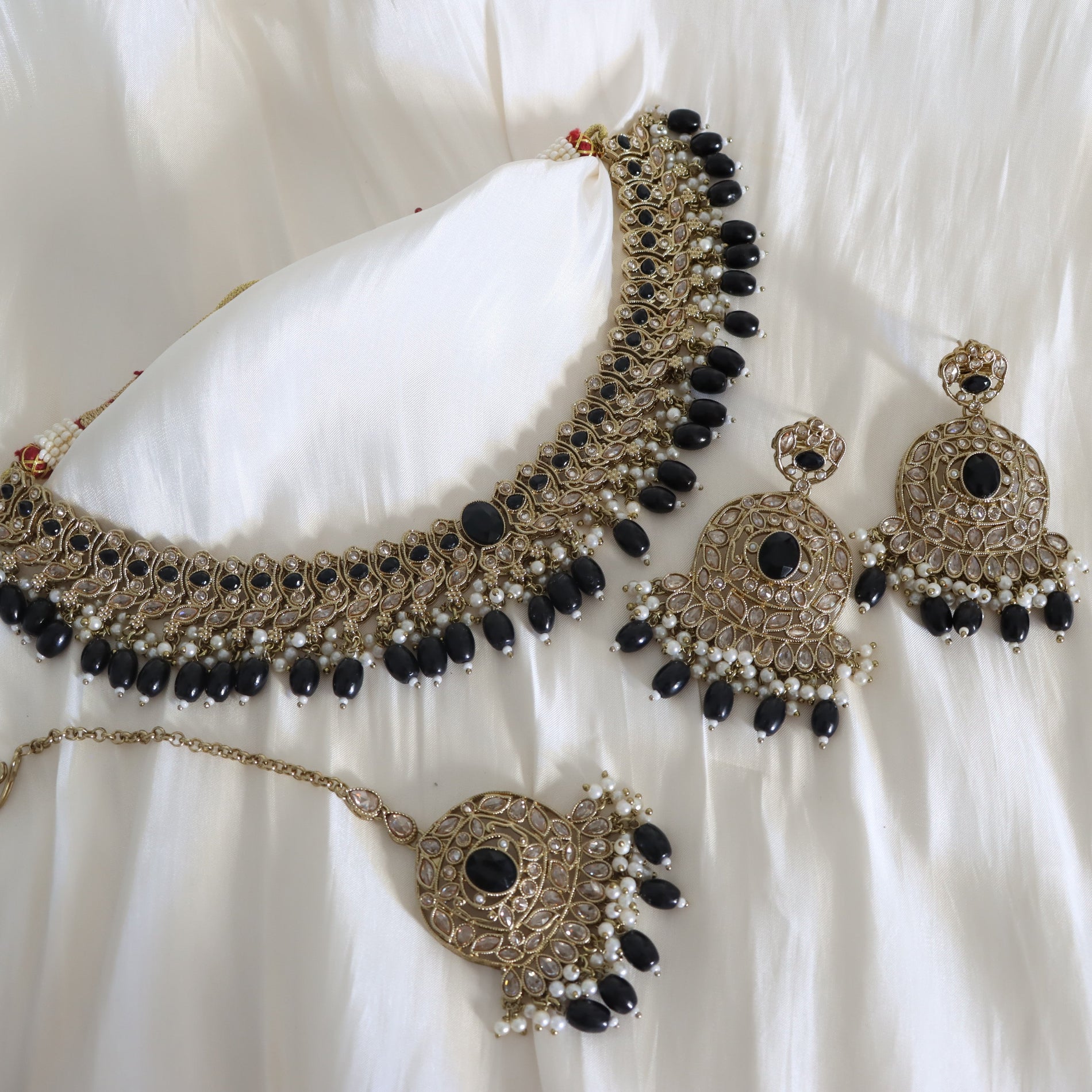 Ornate necklace and earrings with black stones on a white fabric background