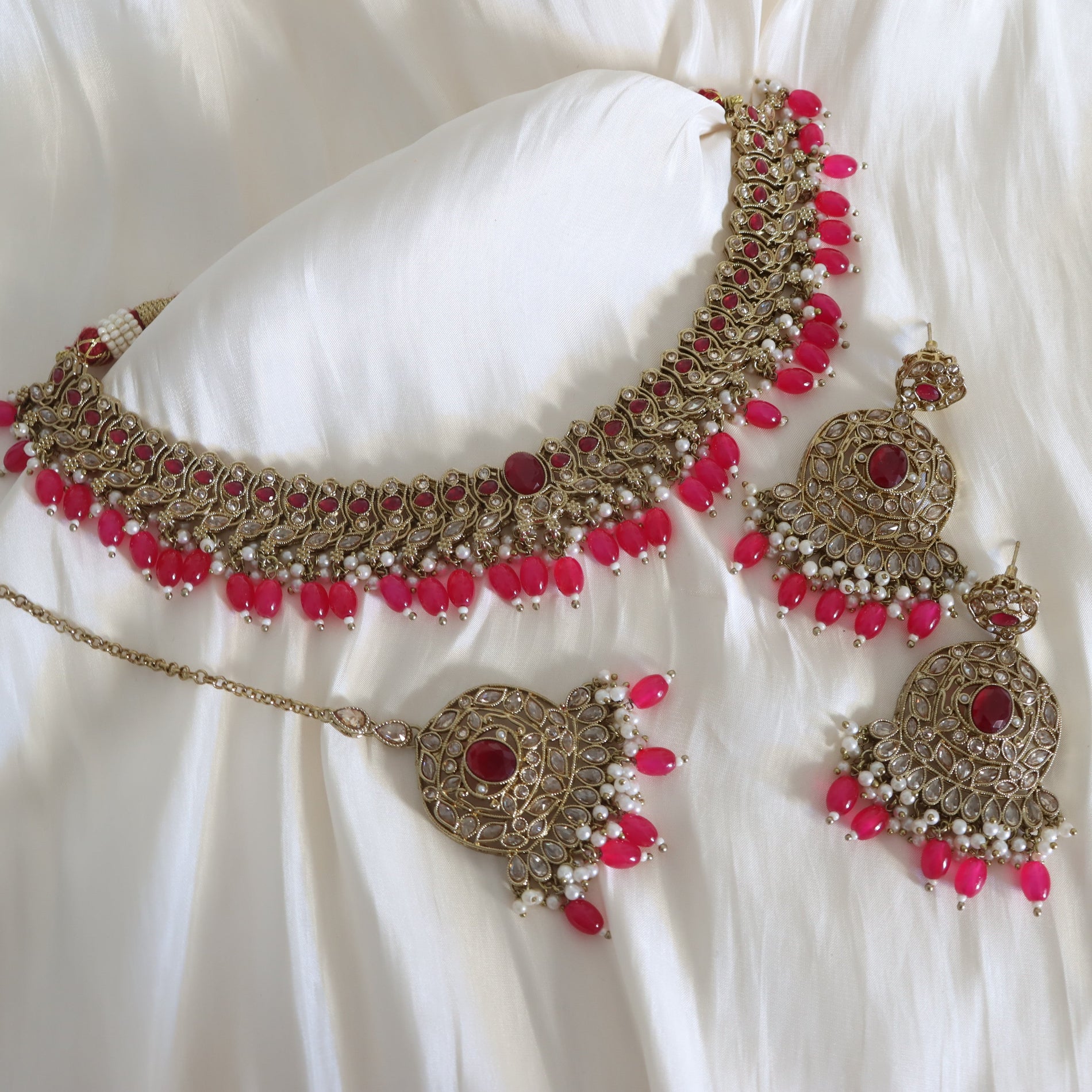 Ornate necklace and earrings with pink beads on a white fabric background