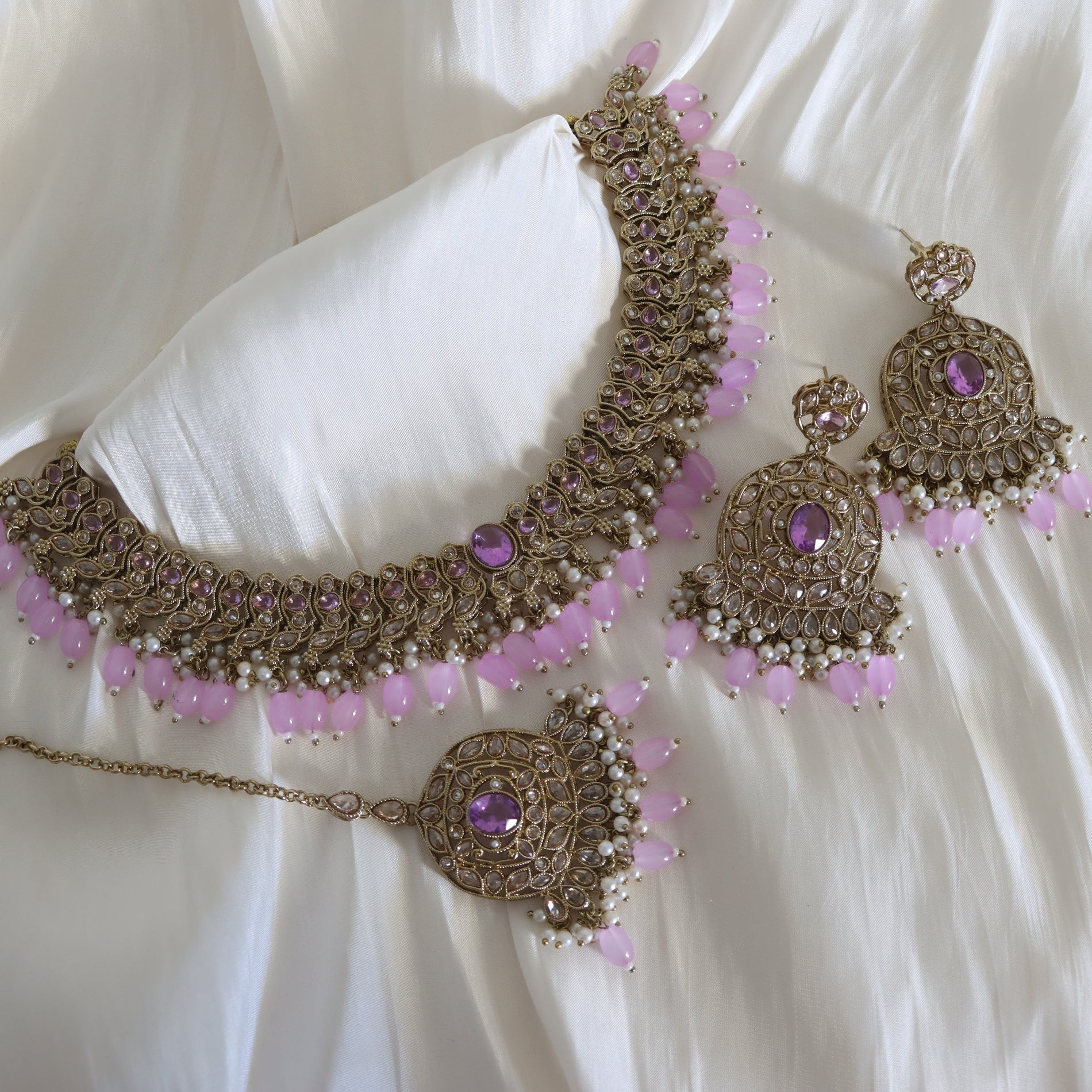 Ornate necklace and earrings with pink beads on a white fabric background