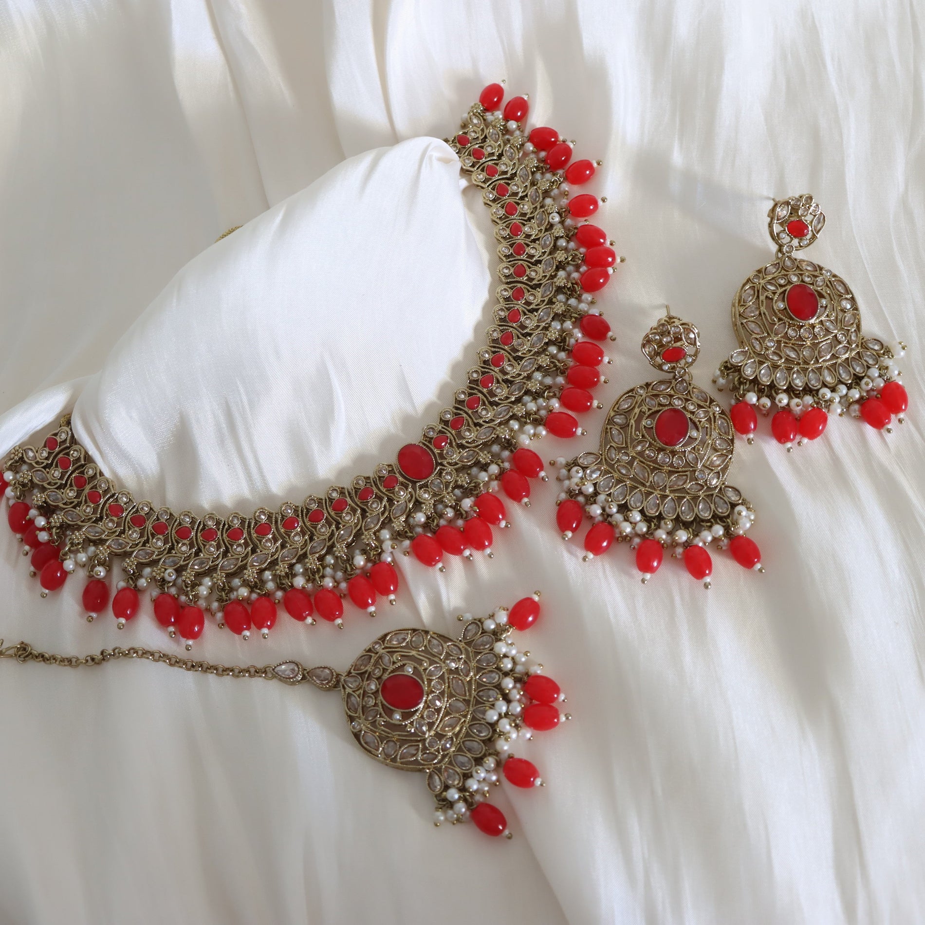 Ornate necklace and earrings with red stones on a white fabric background