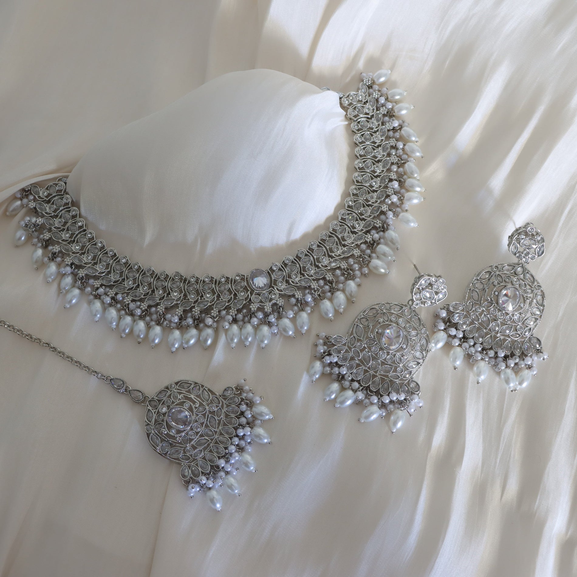 Silver jewelry set with necklace, earrings, and ring on a white fabric background