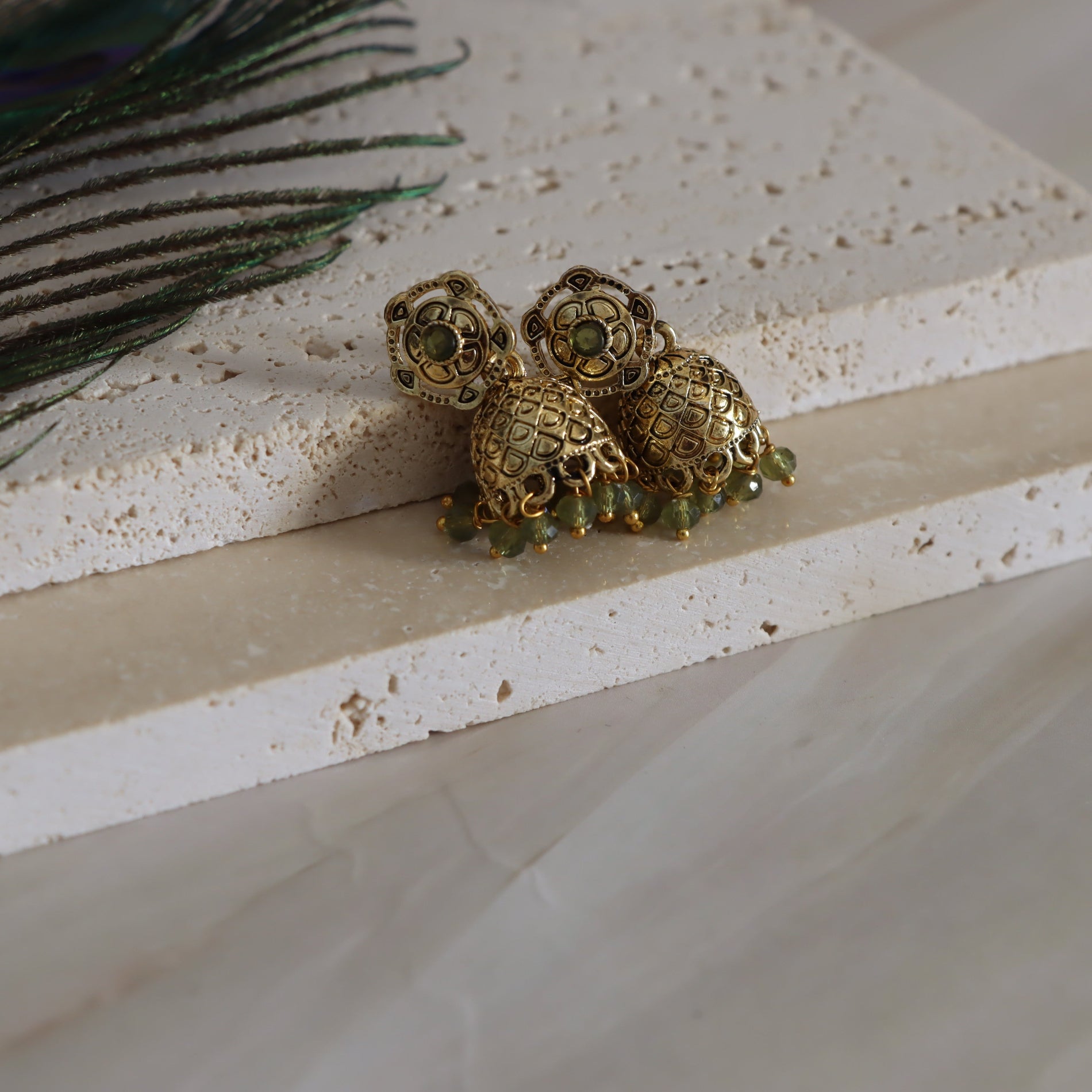 Gold and green earrings on a textured surface