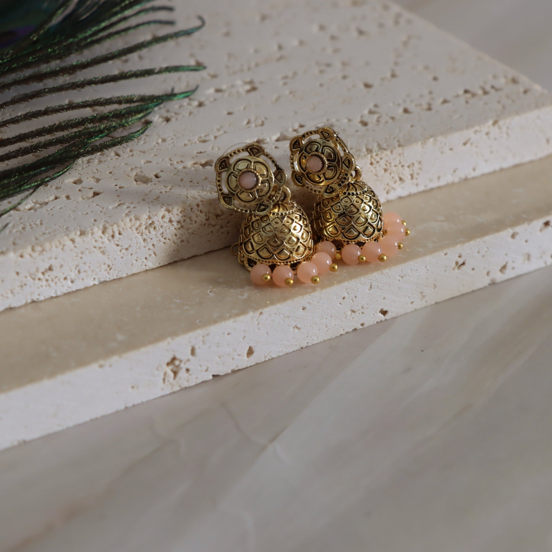 Gold earrings with pink beads on a textured surface