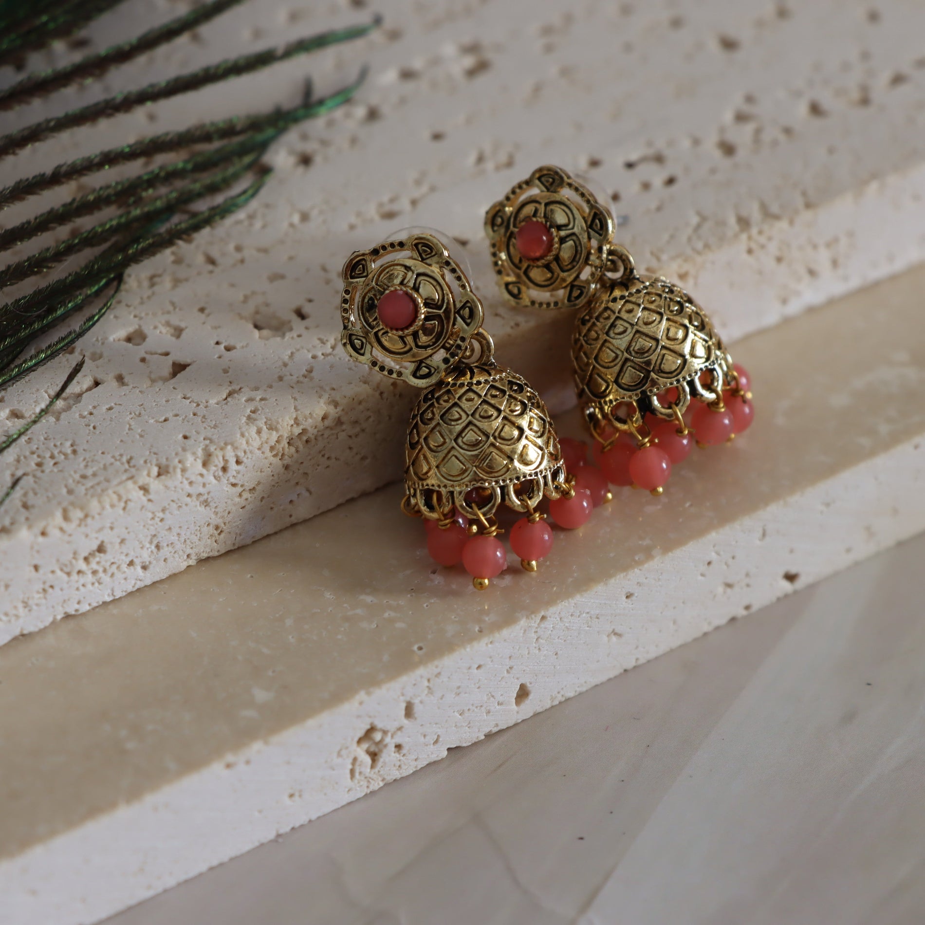 Gold earrings with red beads on a textured surface