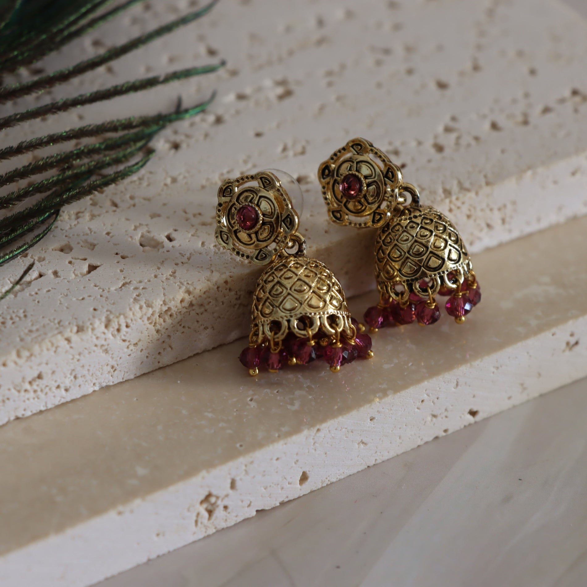 Gold earrings with red gemstones on a textured surface