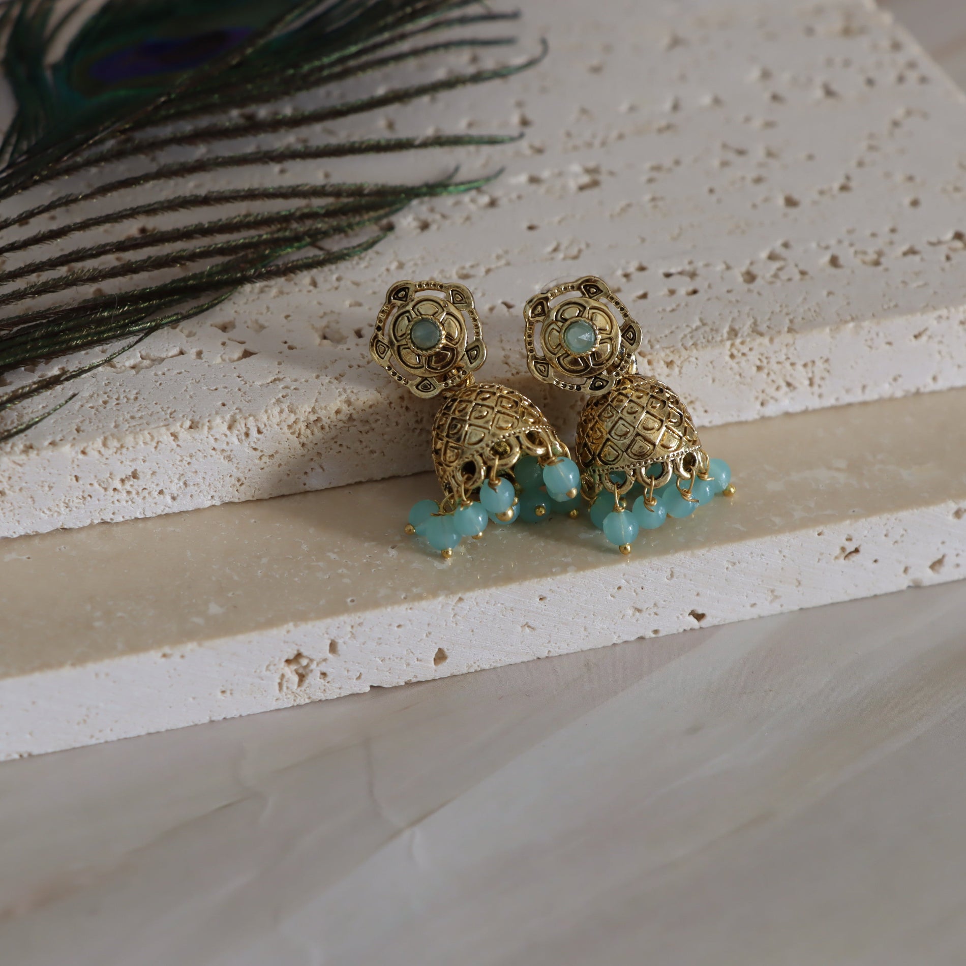 Gold earrings with turquoise beads on a textured surface