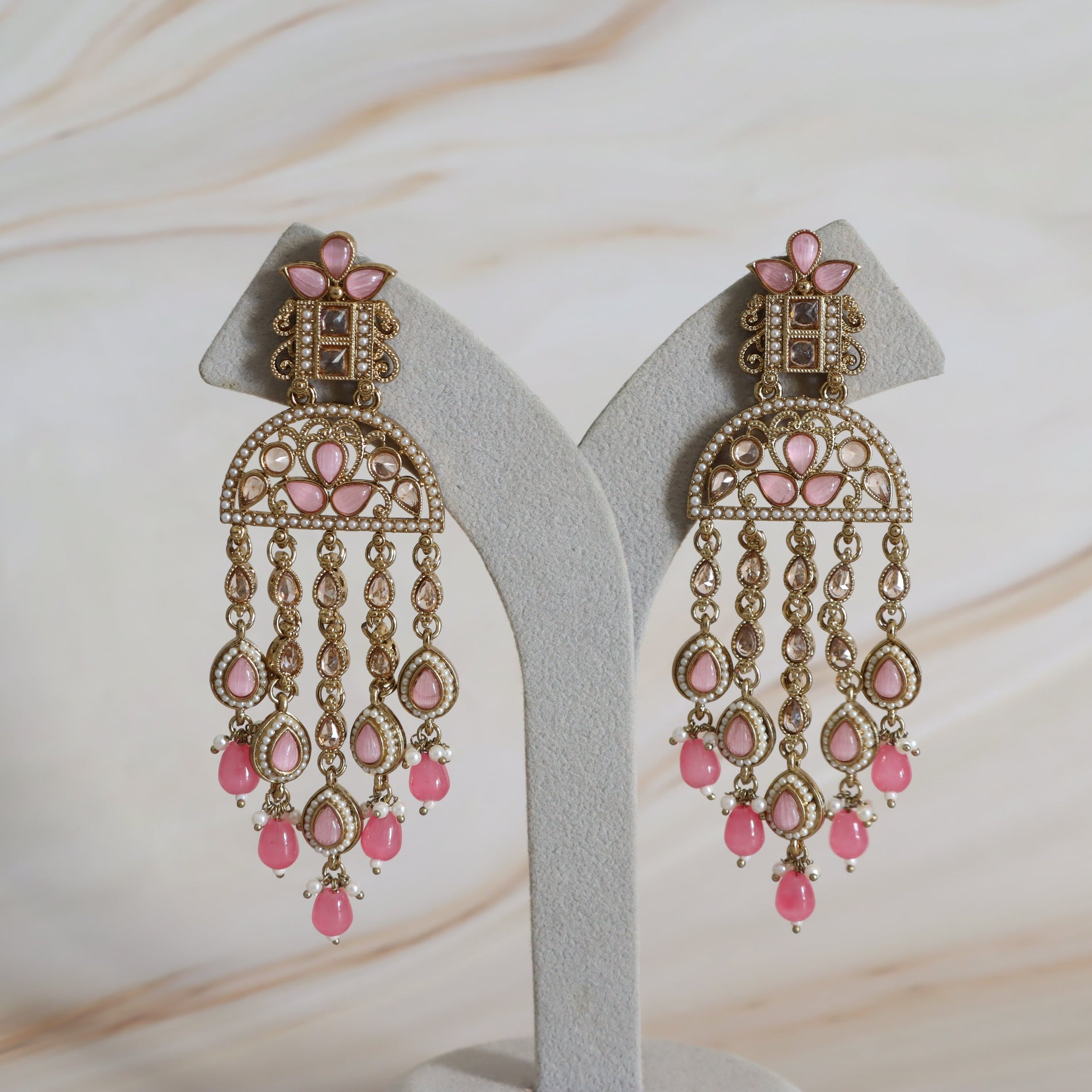 Ornate earrings with pink stones on a white stand against a beige background