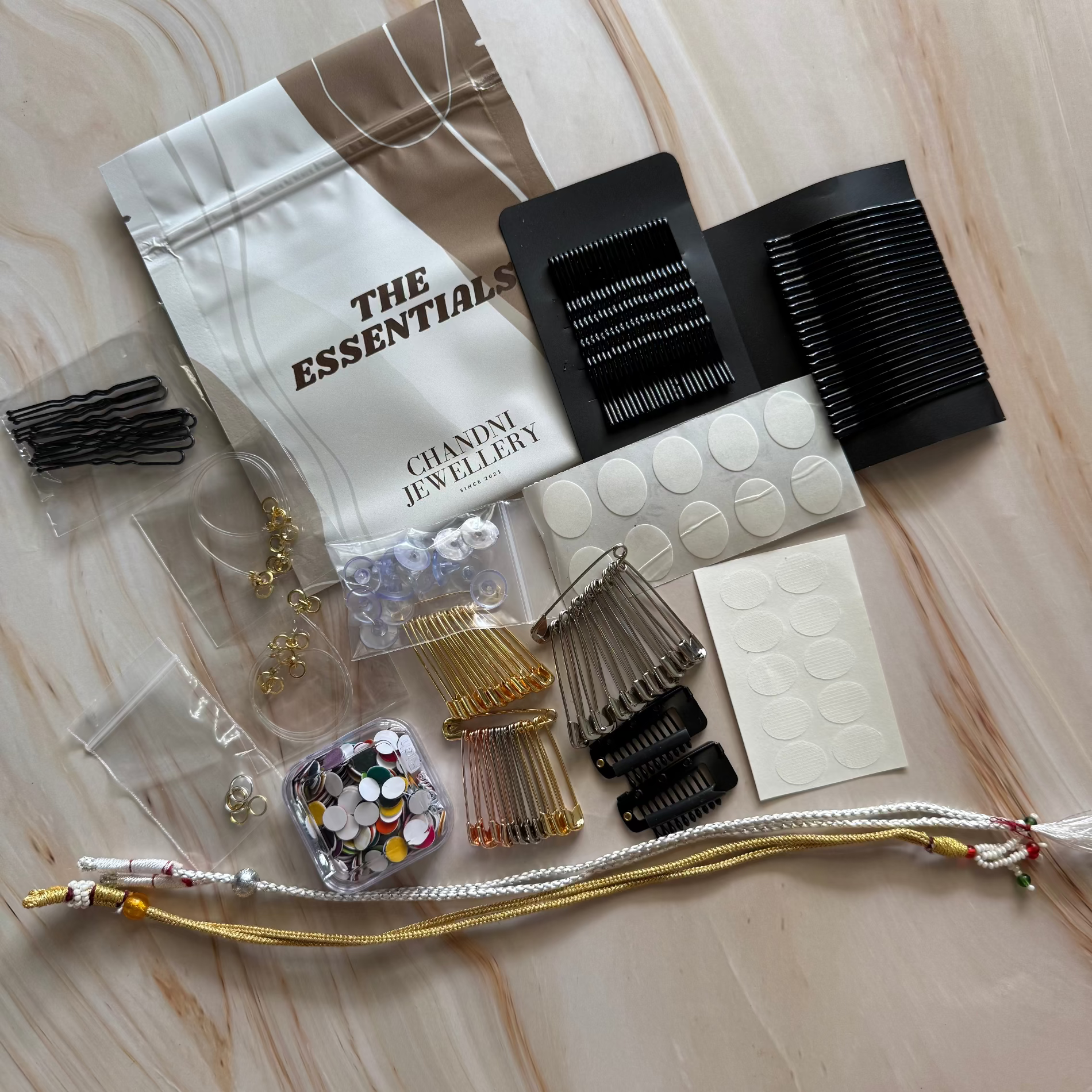 Collection of hair accessories and tools on a marble surface with 'The Essentials' jewelry bag.