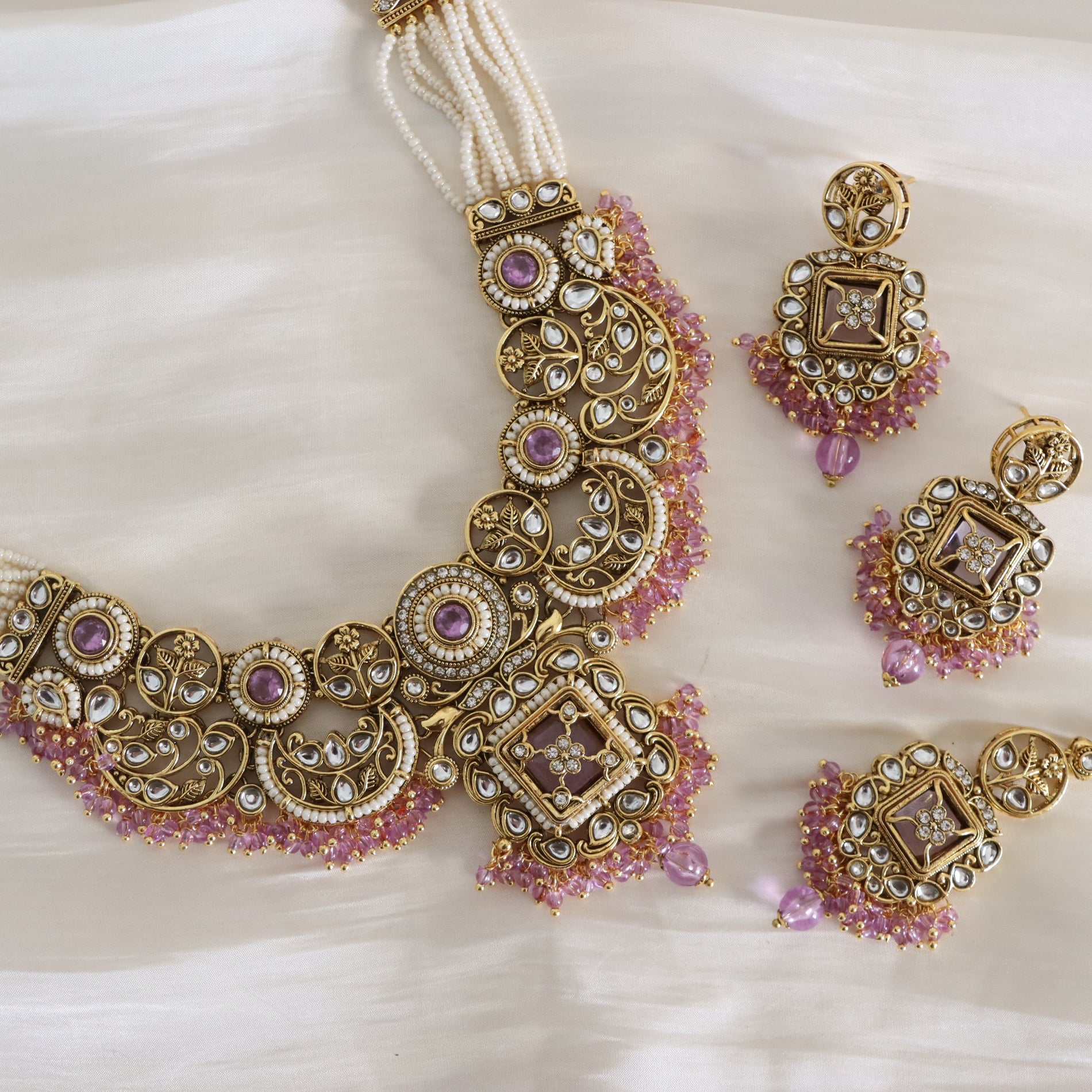 Ornate gold necklace with pink gemstones and matching earrings on a white fabric background