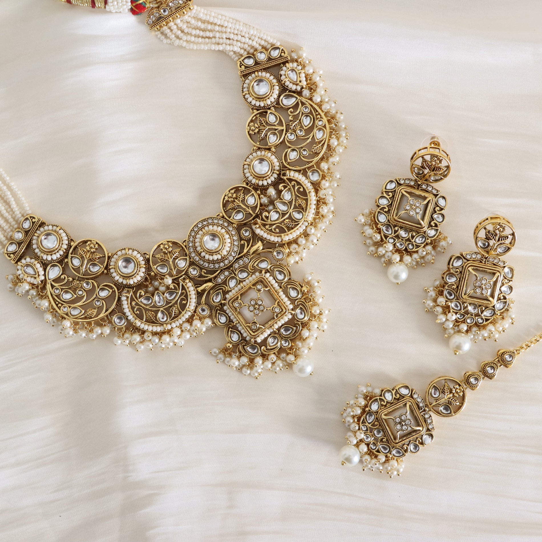 Ornate gold and pearl necklace with matching earrings on a textured white surface