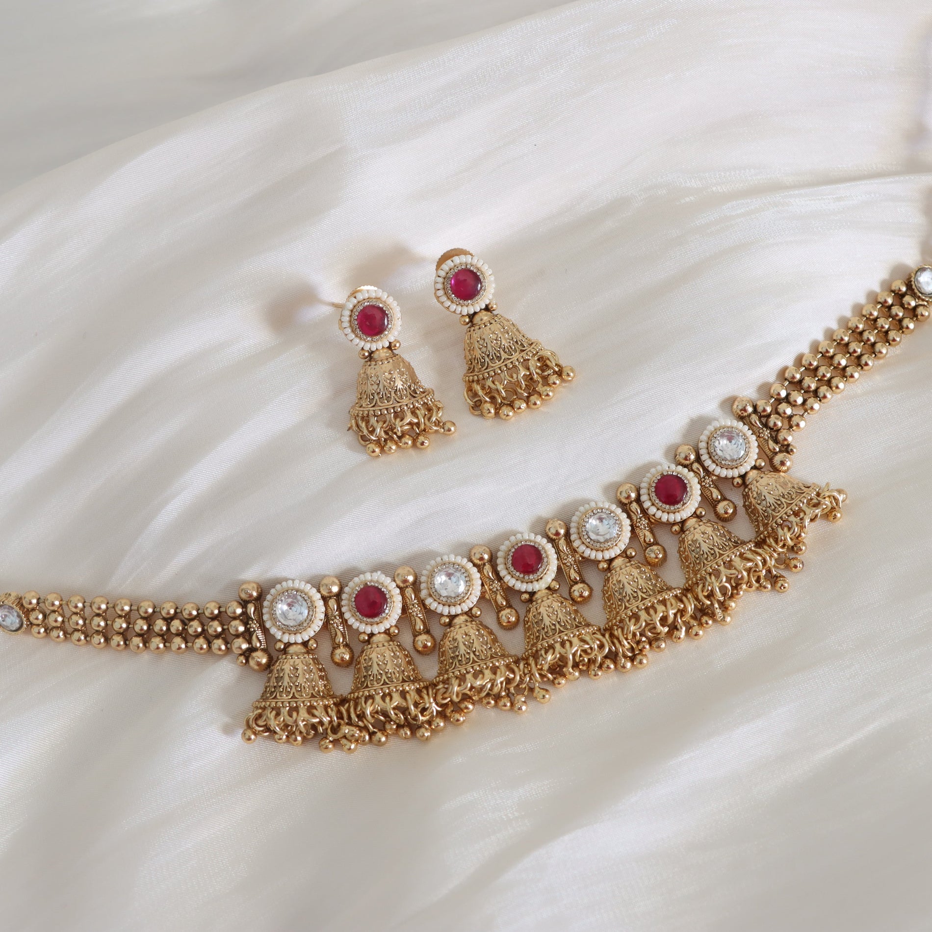 Gold necklace and earrings with red and white stones on a white fabric background