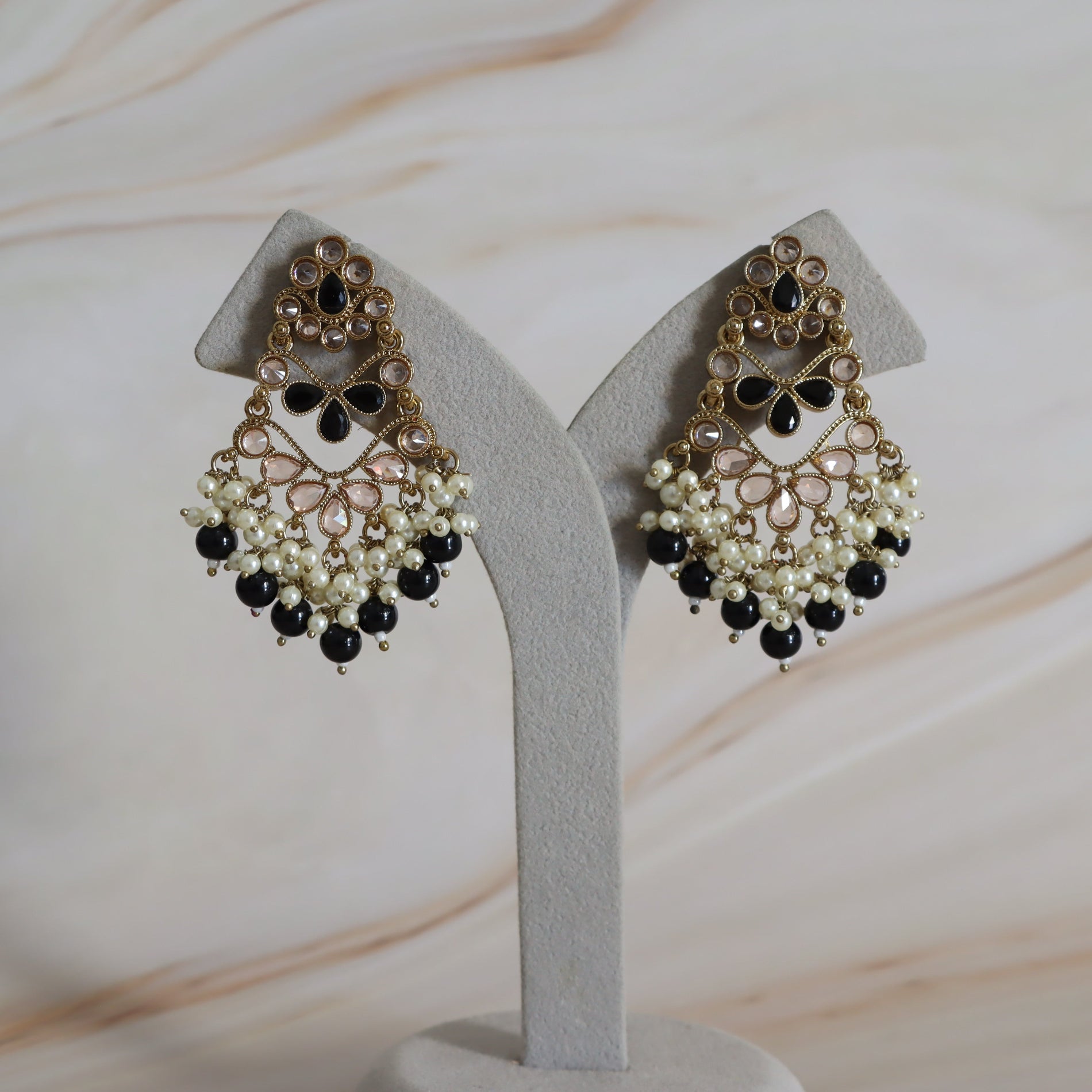 Pair of ornate earrings with black and white beads on a gray stand against a marble background.