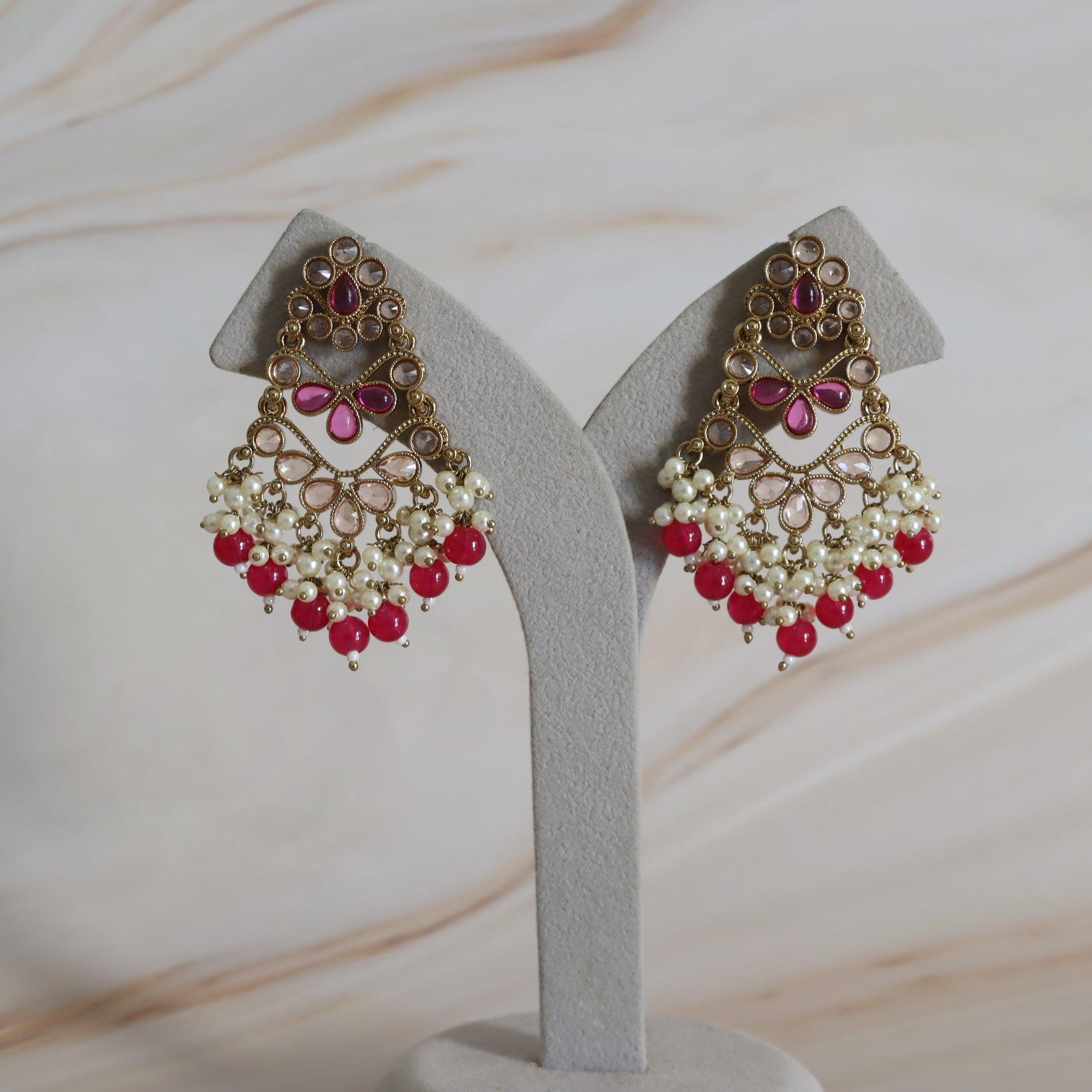 Pair of ornate earrings with red and white stones on a gray stand against a beige background