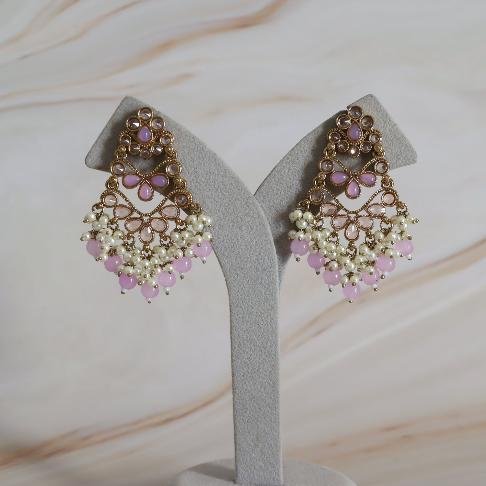 Pair of ornate earrings with pink and white stones on a gray stand against a marble background