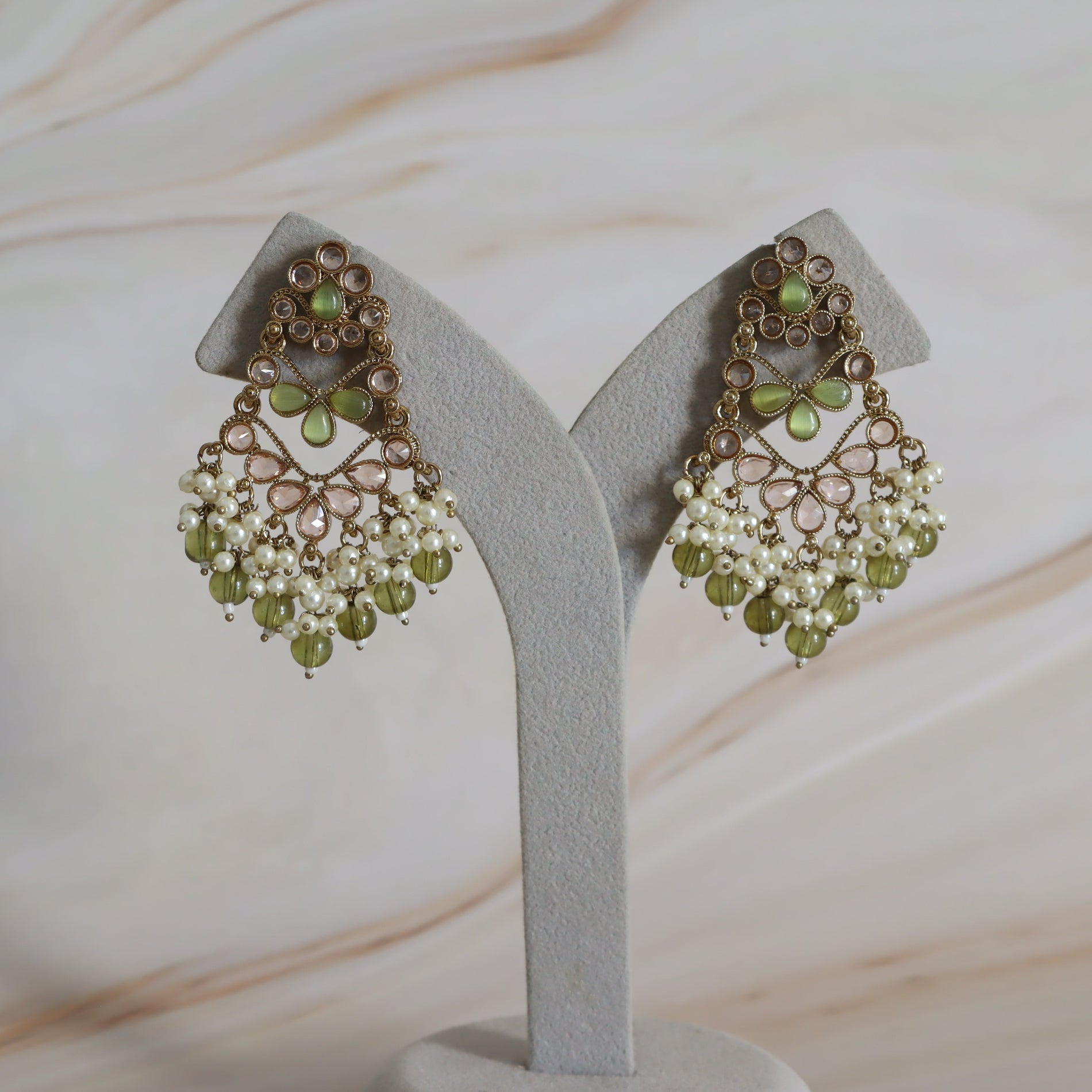 Pair of green and gold earrings on a gray stand with a light background