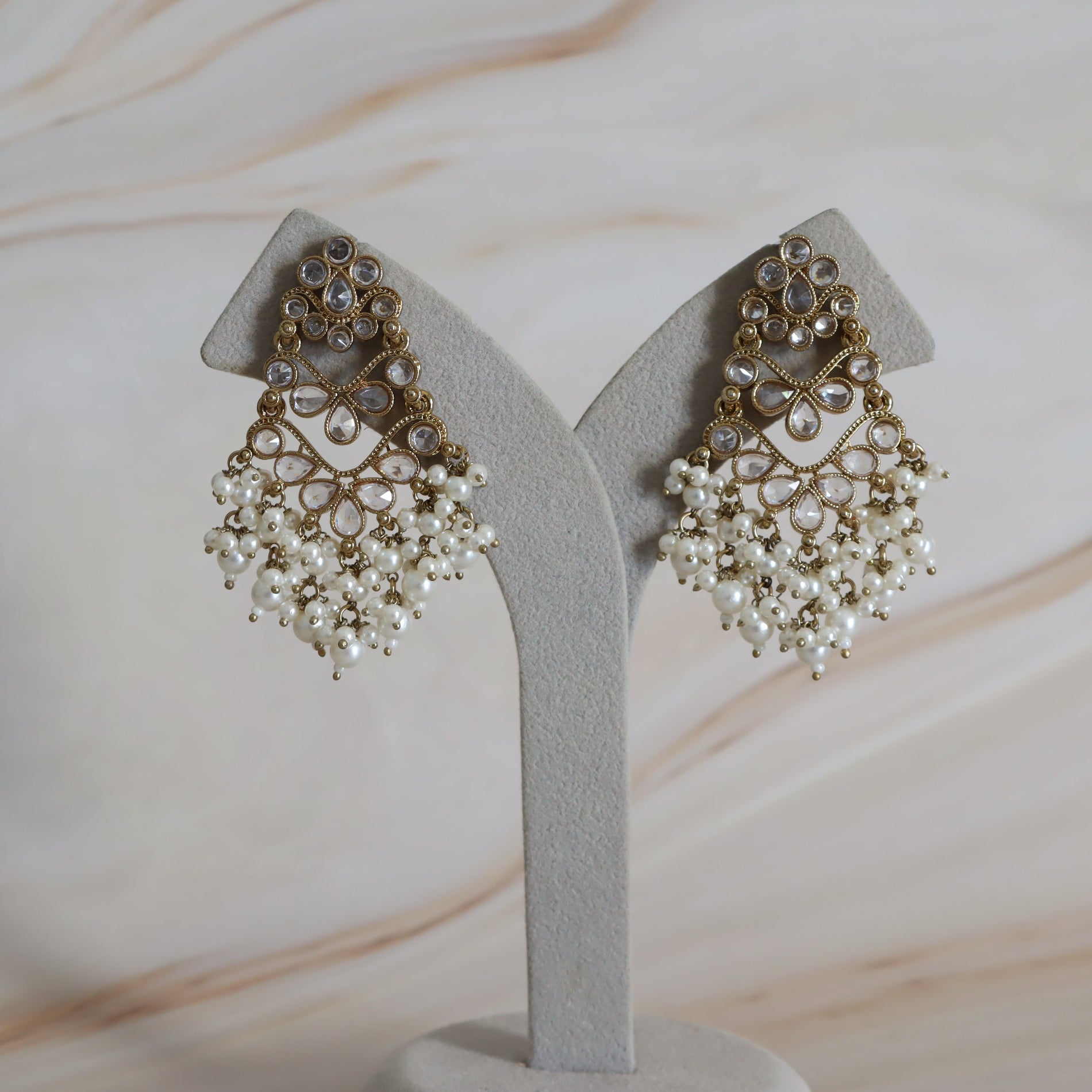 Pair of ornate earrings on a gray stand with a neutral background