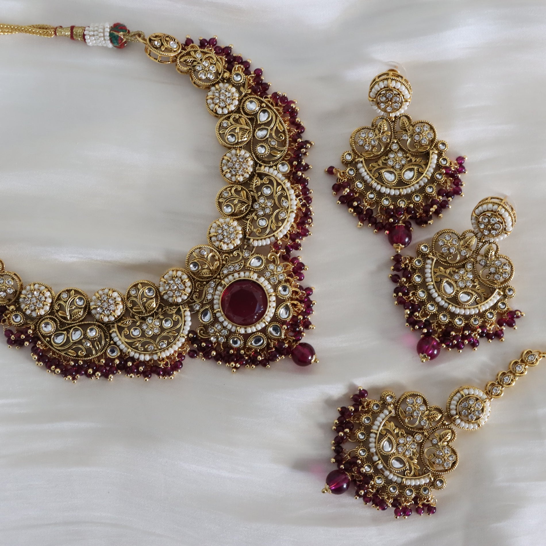 Ornate gold necklace with red stones and matching earrings on a white fabric background