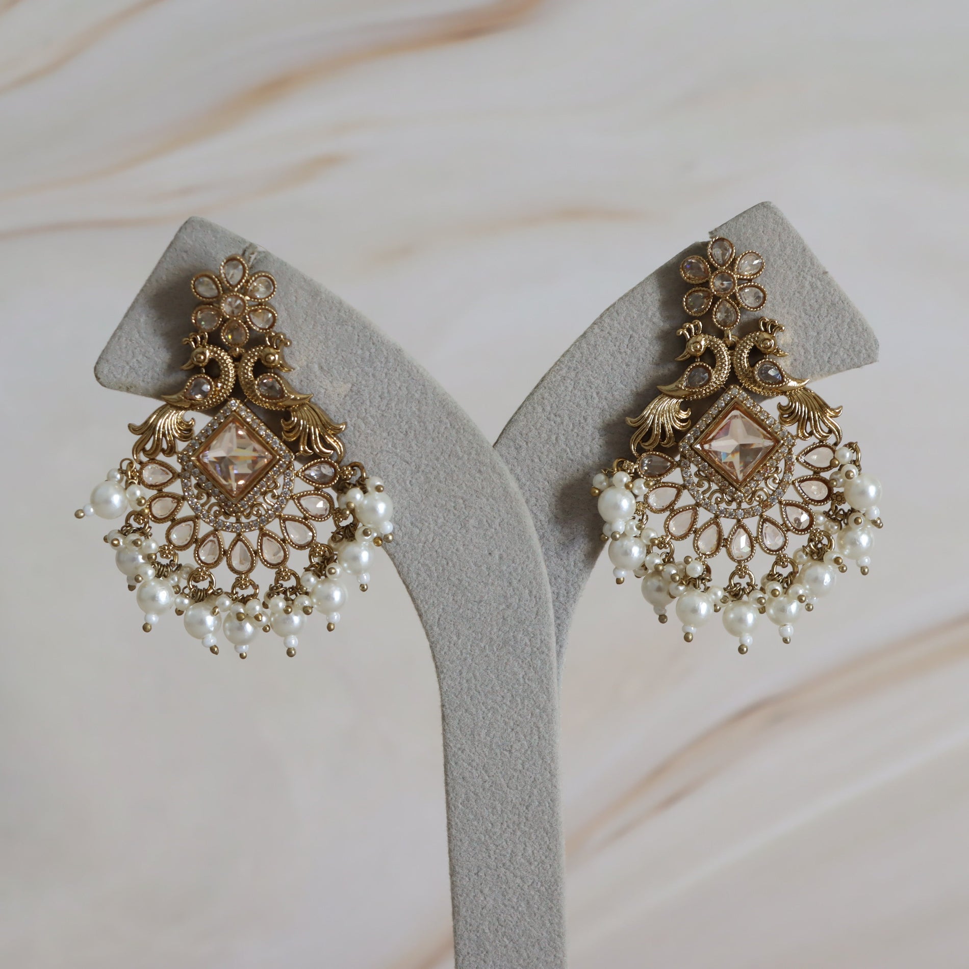 Ornate gold and pearl earrings on a gray stand with a soft beige background