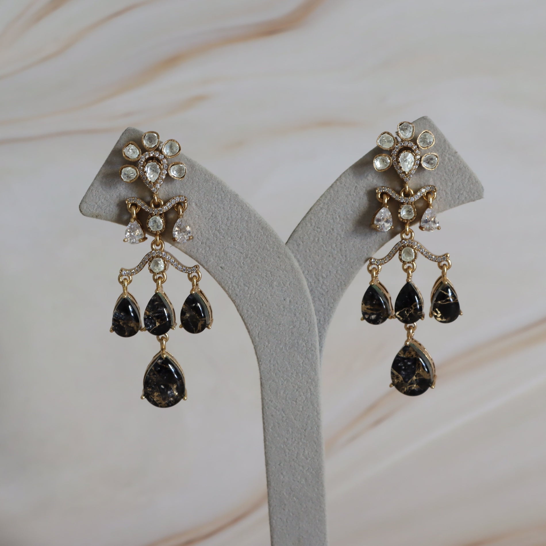 Pair of gold and black teardrop earrings on a gray stand with a neutral background