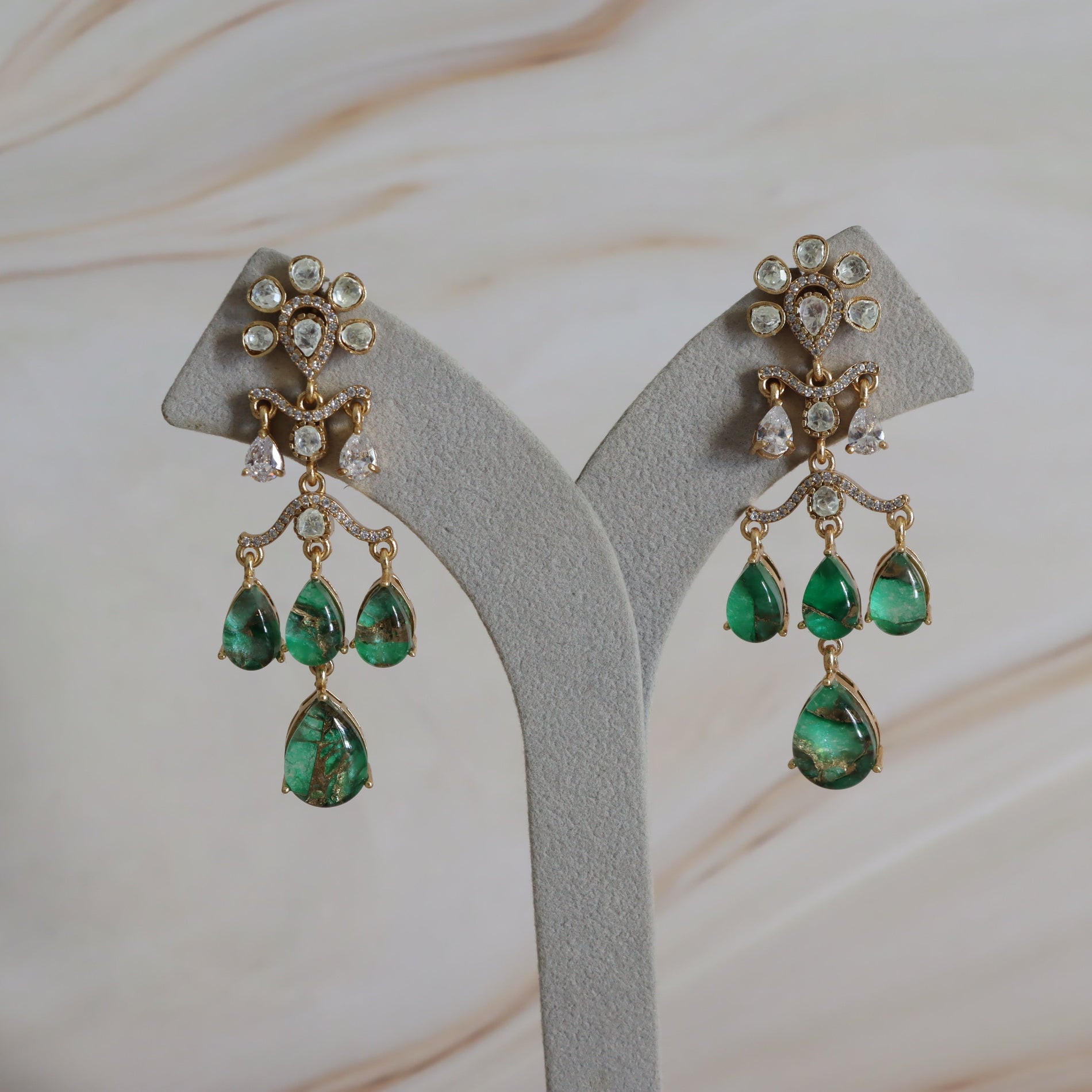 Pair of emerald and diamond earrings on a gray stand with a soft beige background