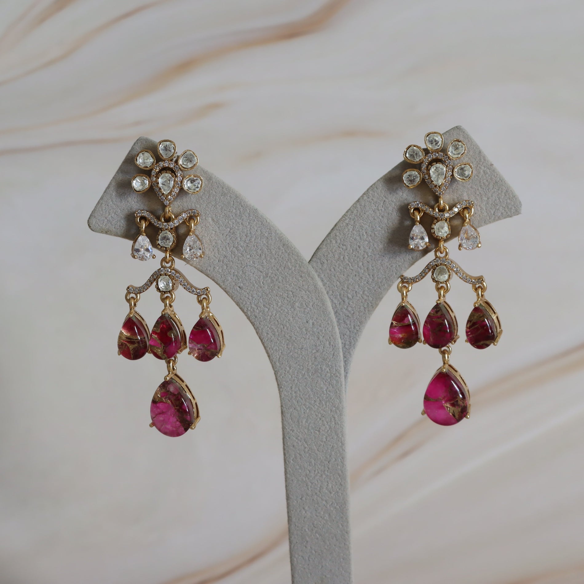 Pair of earrings with hot pink gemstones and gold accents on a gray stand.