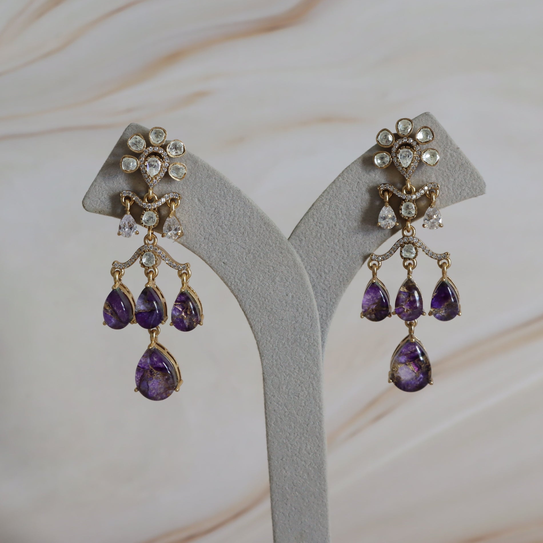 Pair of purple teardrop earrings on a gray stand with a soft beige background