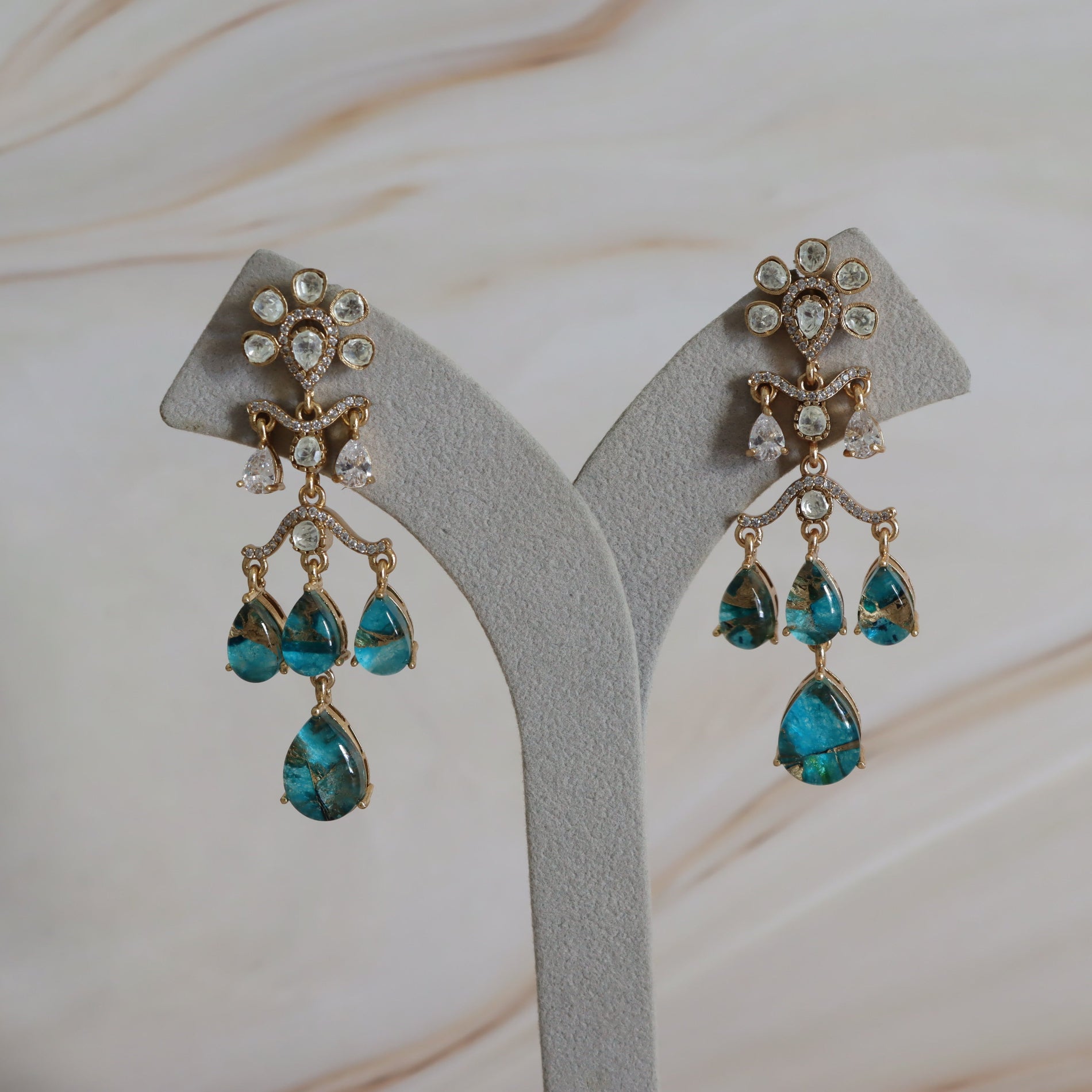 Pair of earrings with turquoise stones on a gray stand.