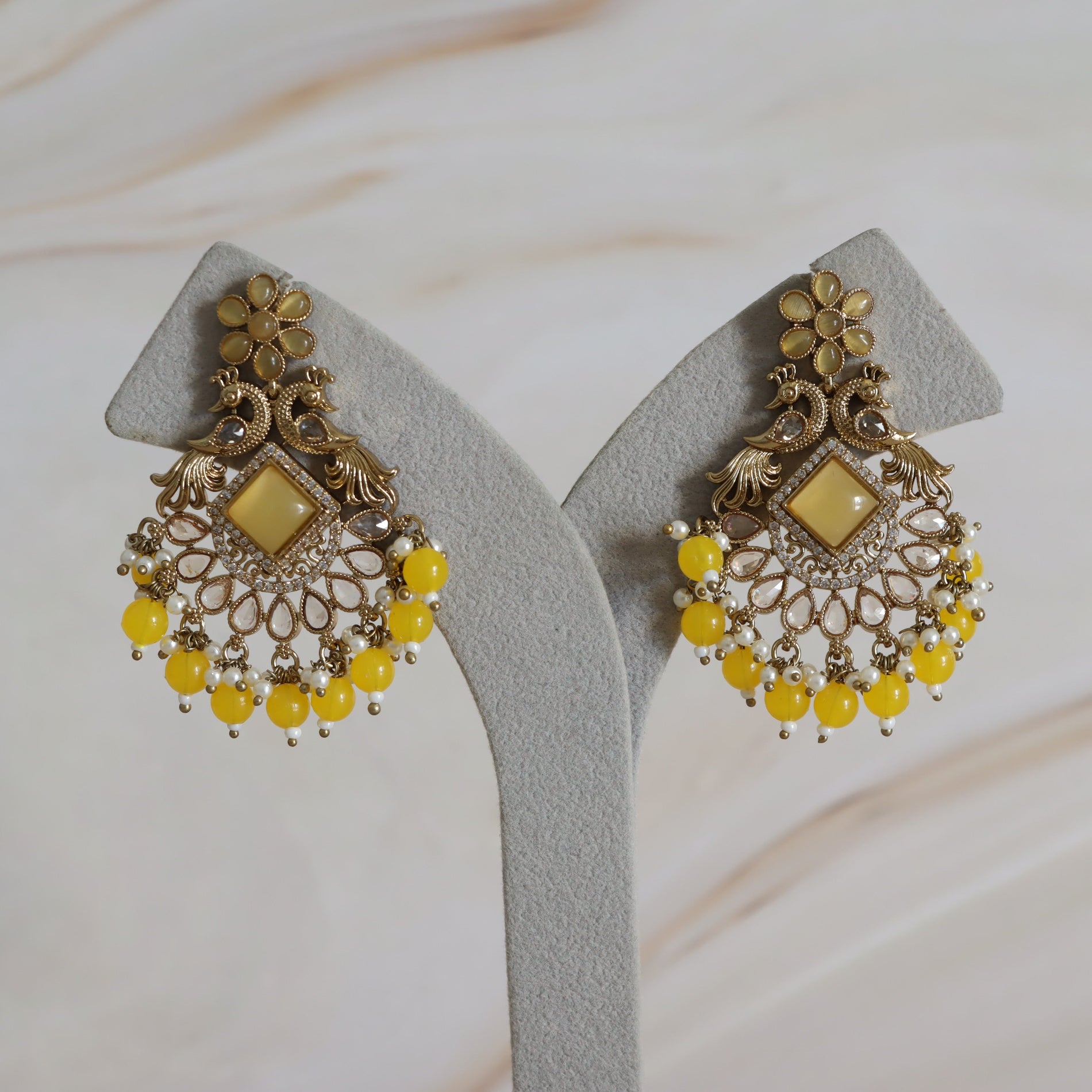Pair of ornate earrings with yellow beads on a gray stand.