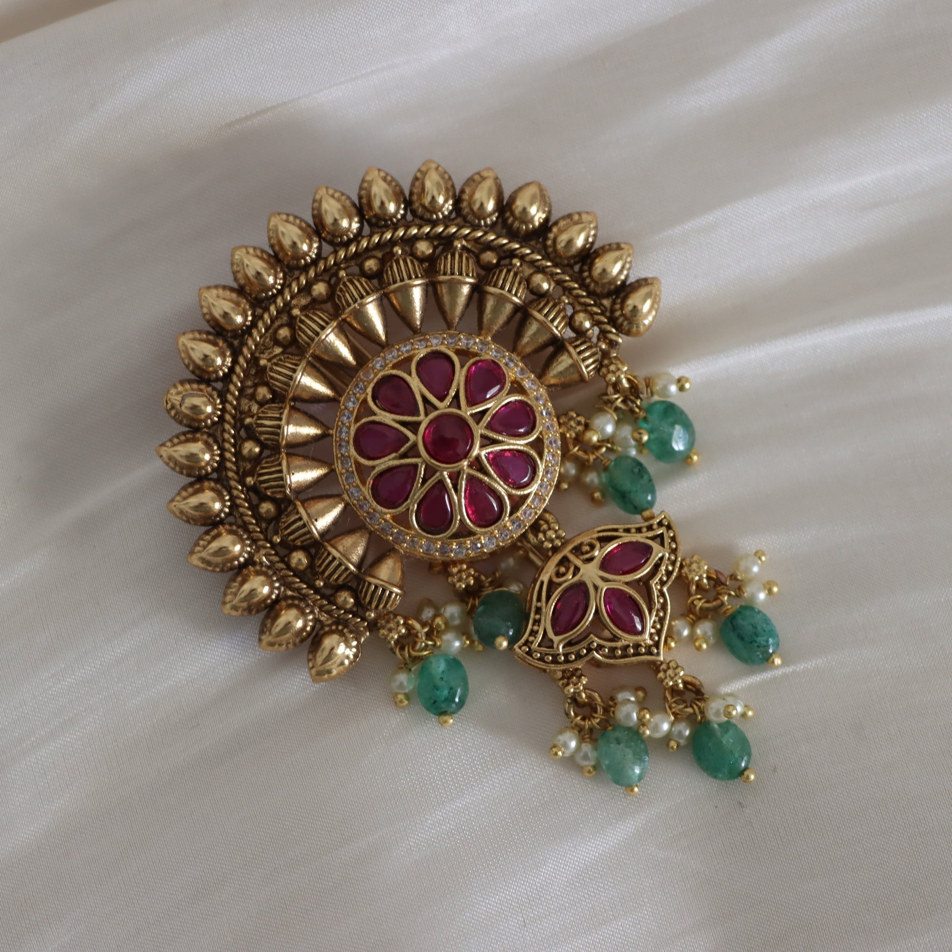 Decorative gold earring with red and green stones on a white fabric background
