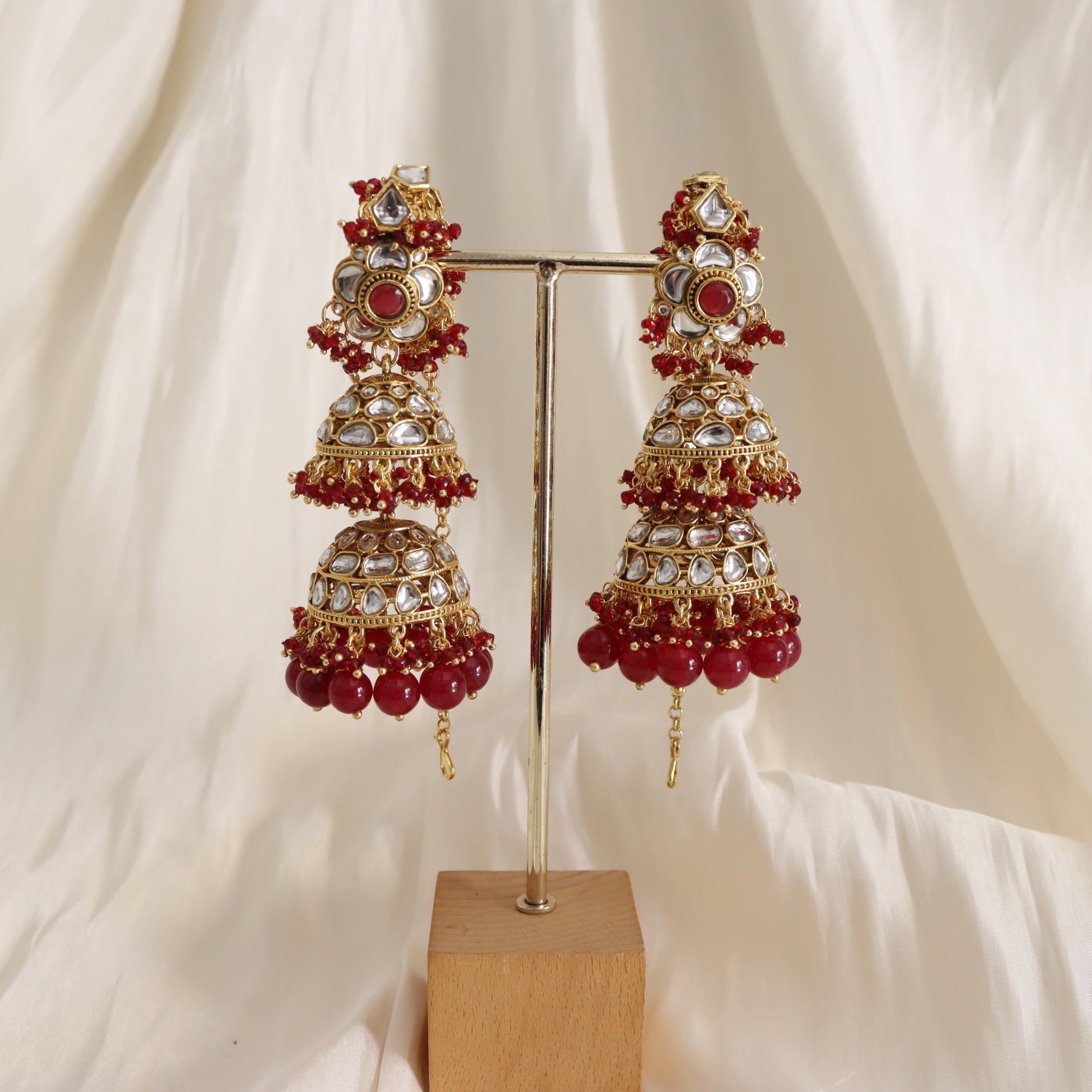 Ornate earrings with red and gold details on a stand against a soft white background