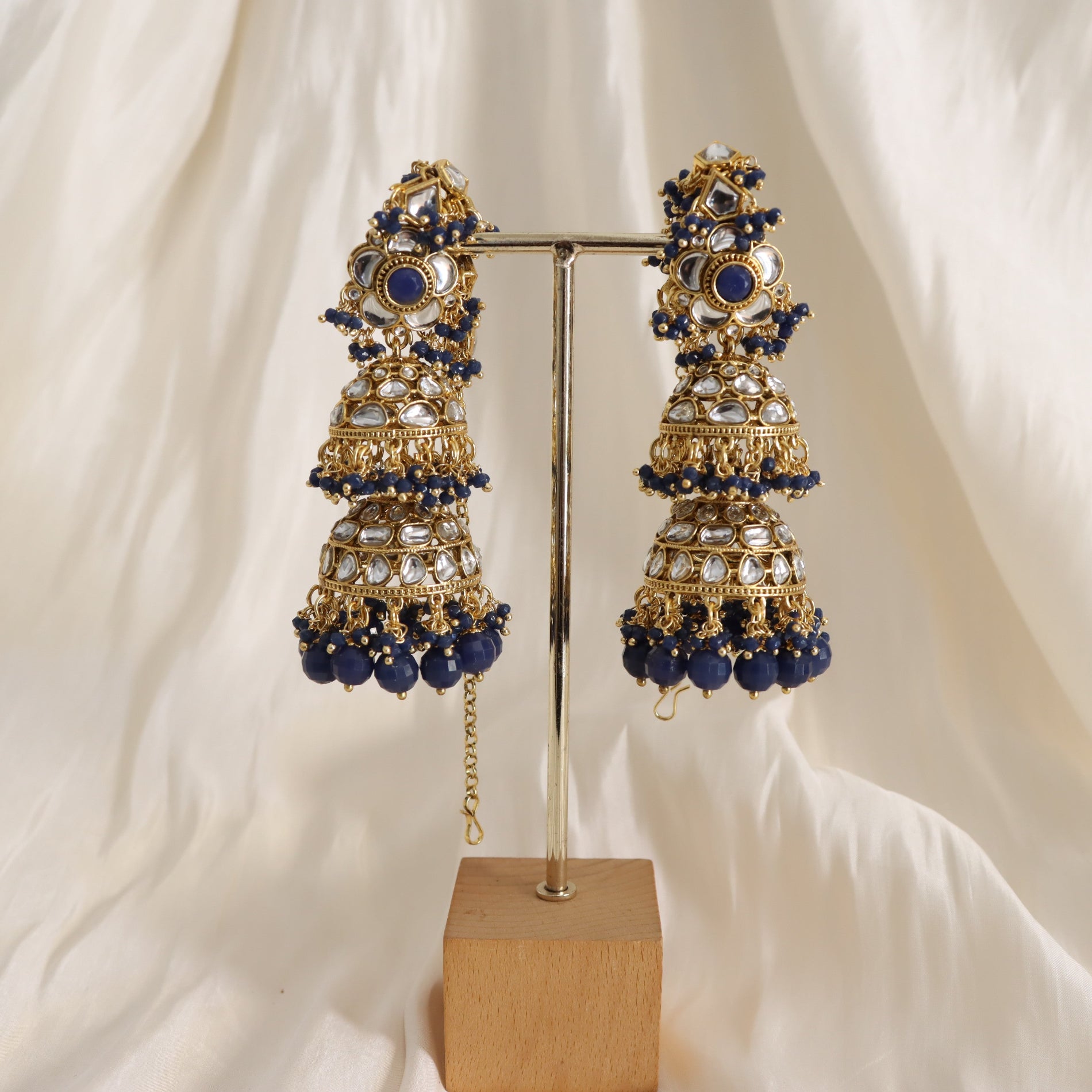 Pair of gold and blue earrings on a stand with a white fabric background