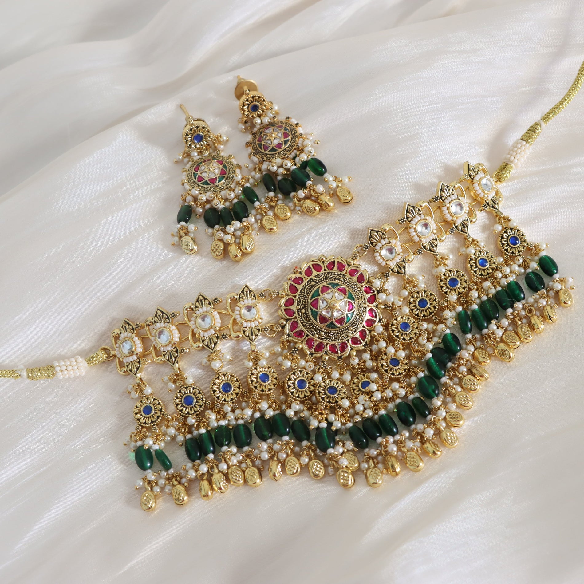 Ornate gold, green, and red jewelry set on a white fabric background