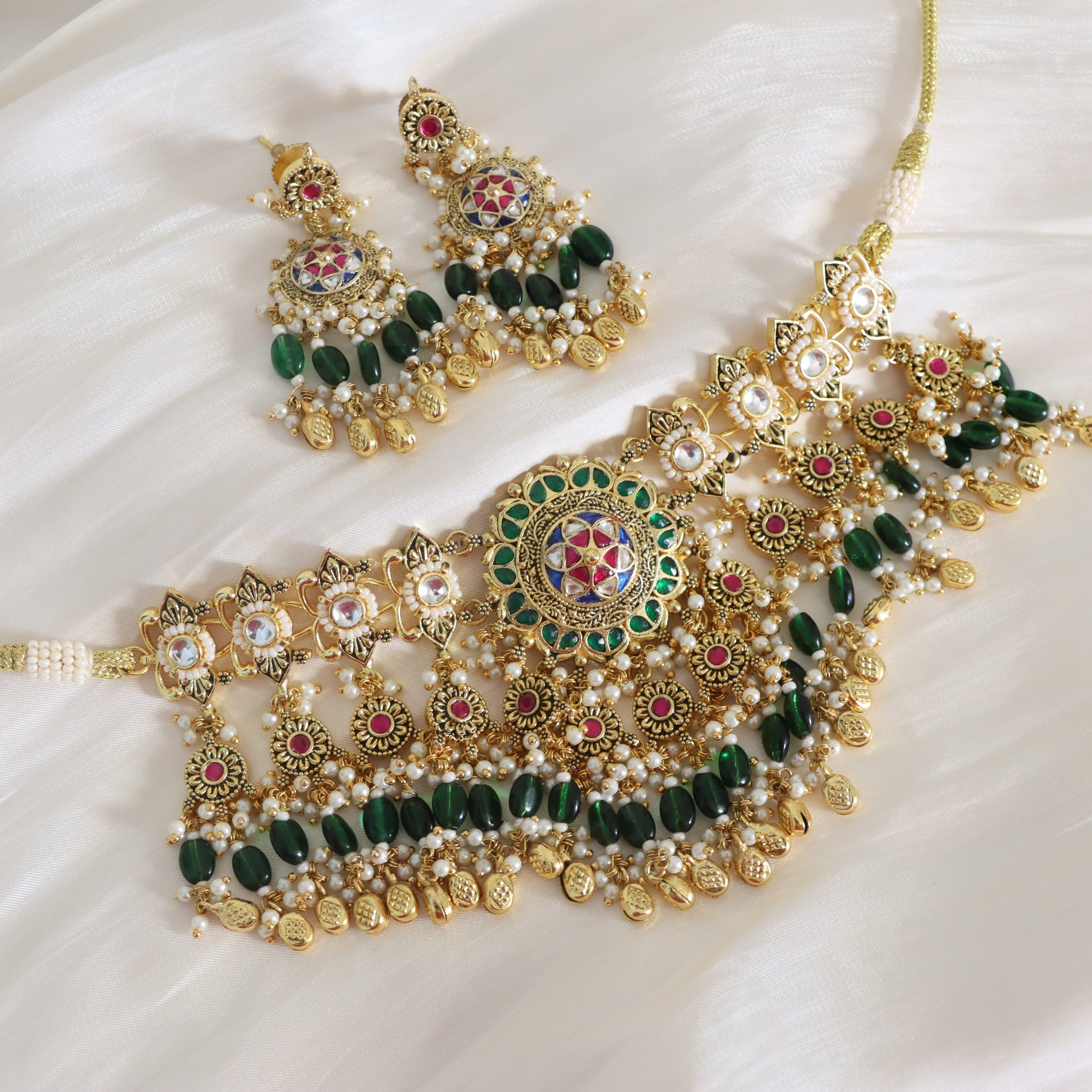 Ornate gold, green, and red jewelry set on a white fabric background