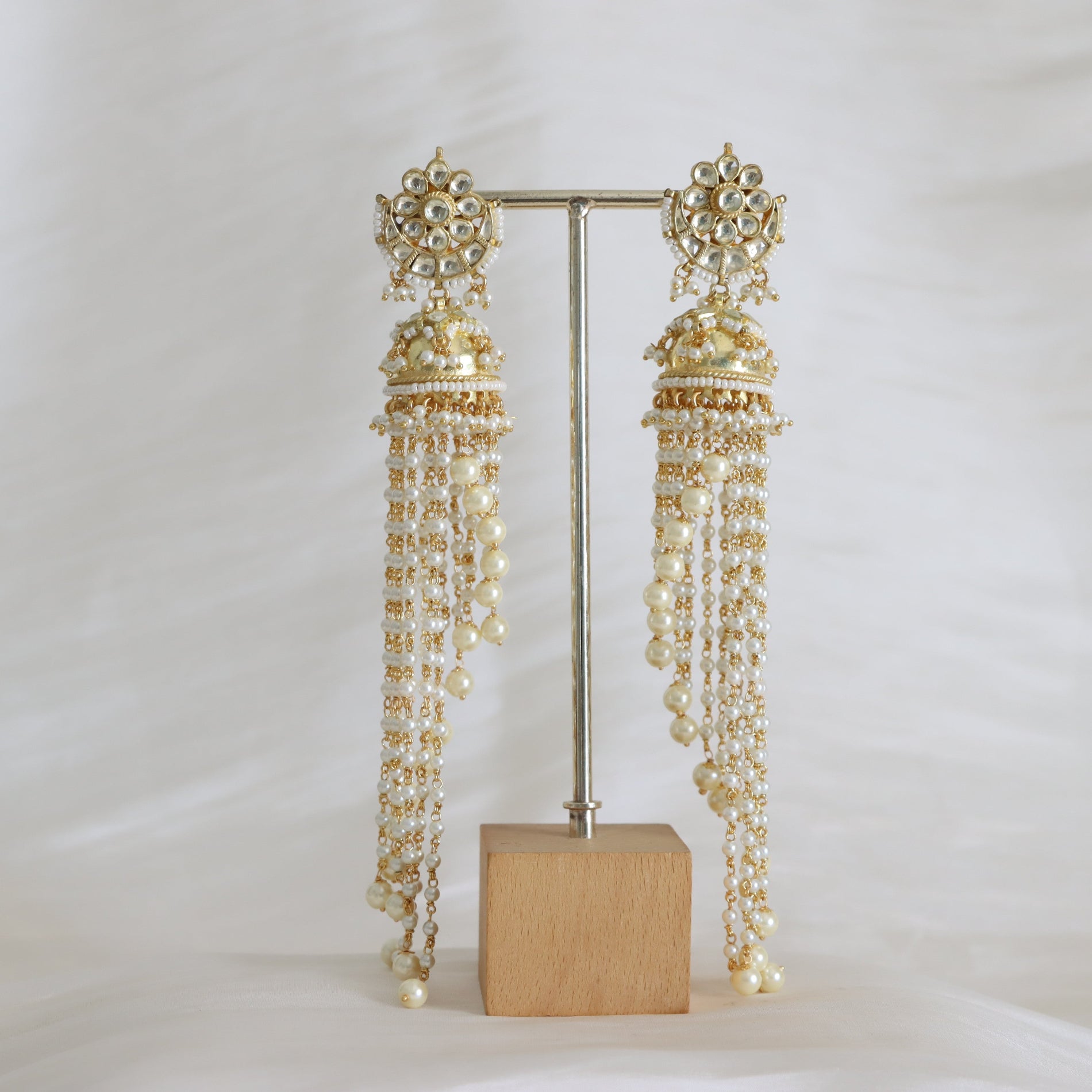 Pair of long, beaded earrings on a stand with a white background