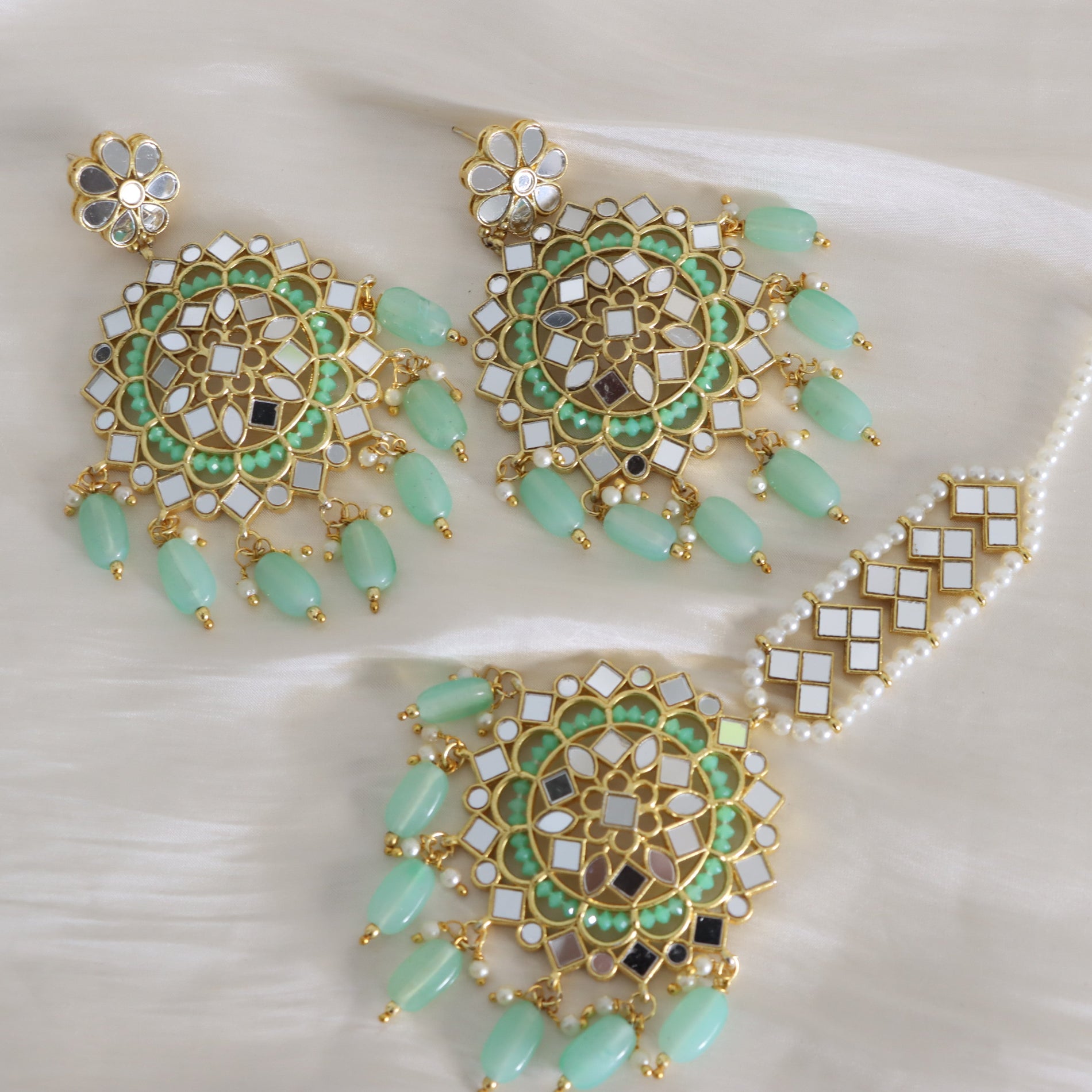 Gold-plated Indian bridal jewelry set featuring a matching necklace, earrings, and a choker with intricate green and white inlay patterns, bead tassels, and pearl-like accents, displayed on a soft white fabric background.