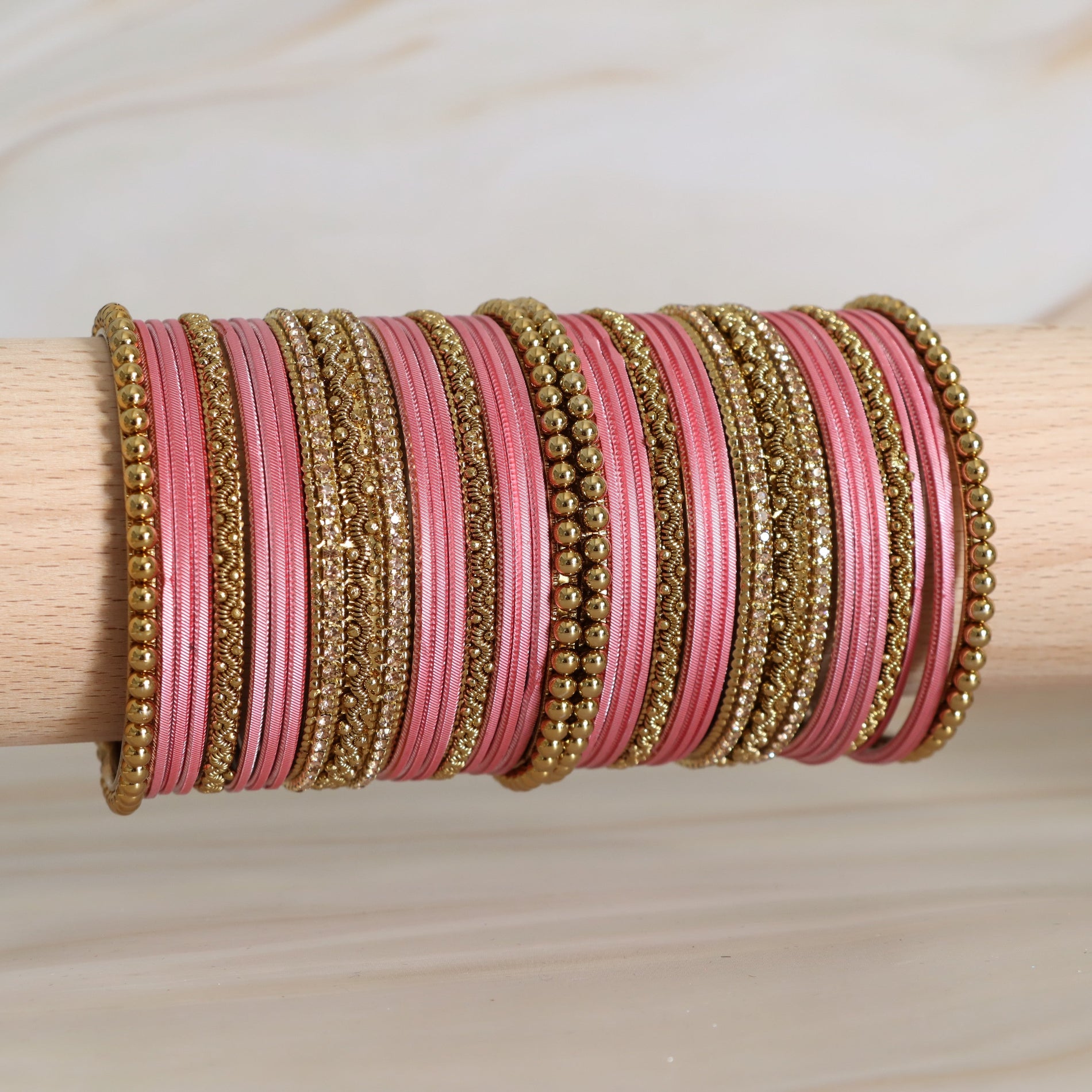 Pink and gold bangles on a wooden stick against a neutral background