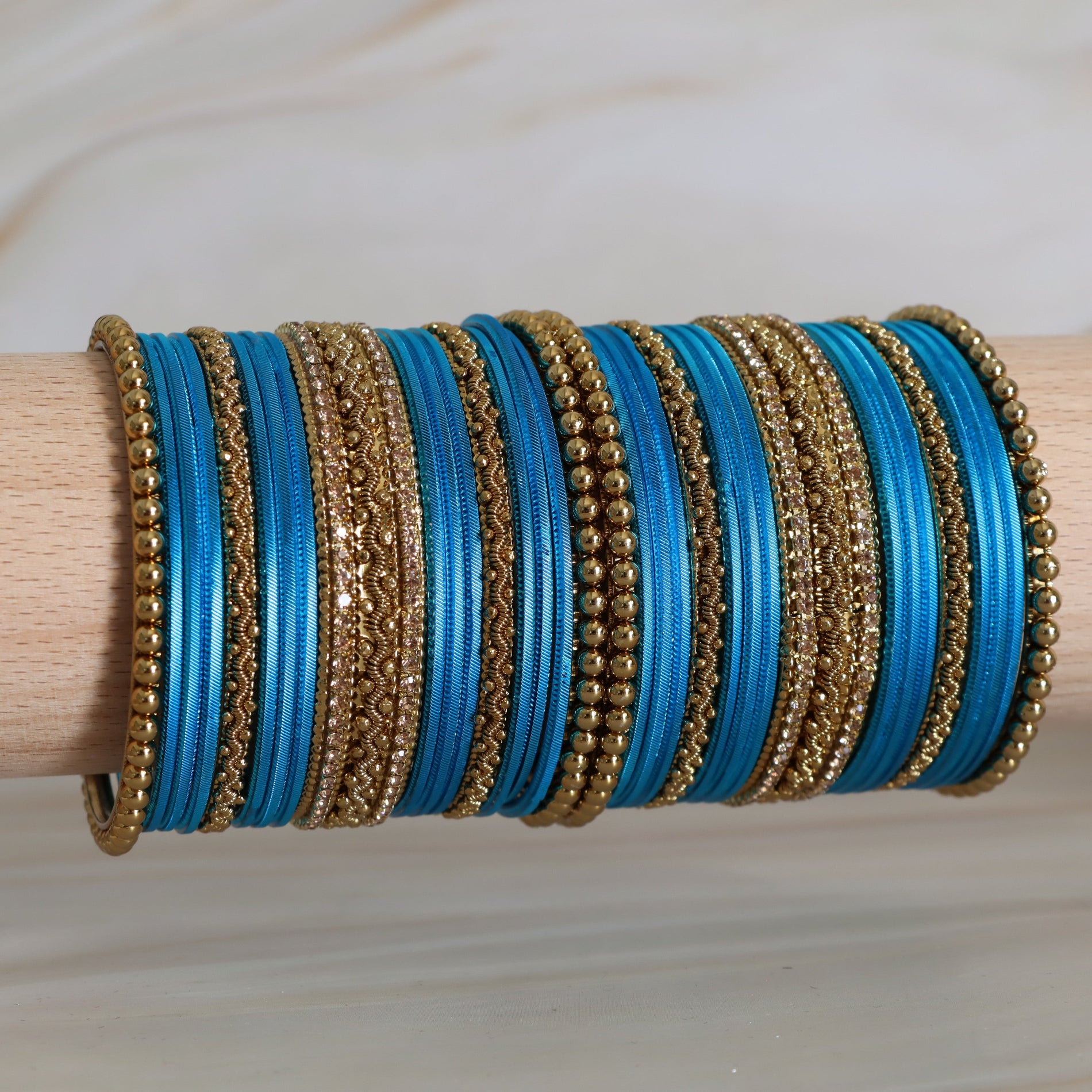 Set of blue and gold bangles on a wooden stick against a neutral background