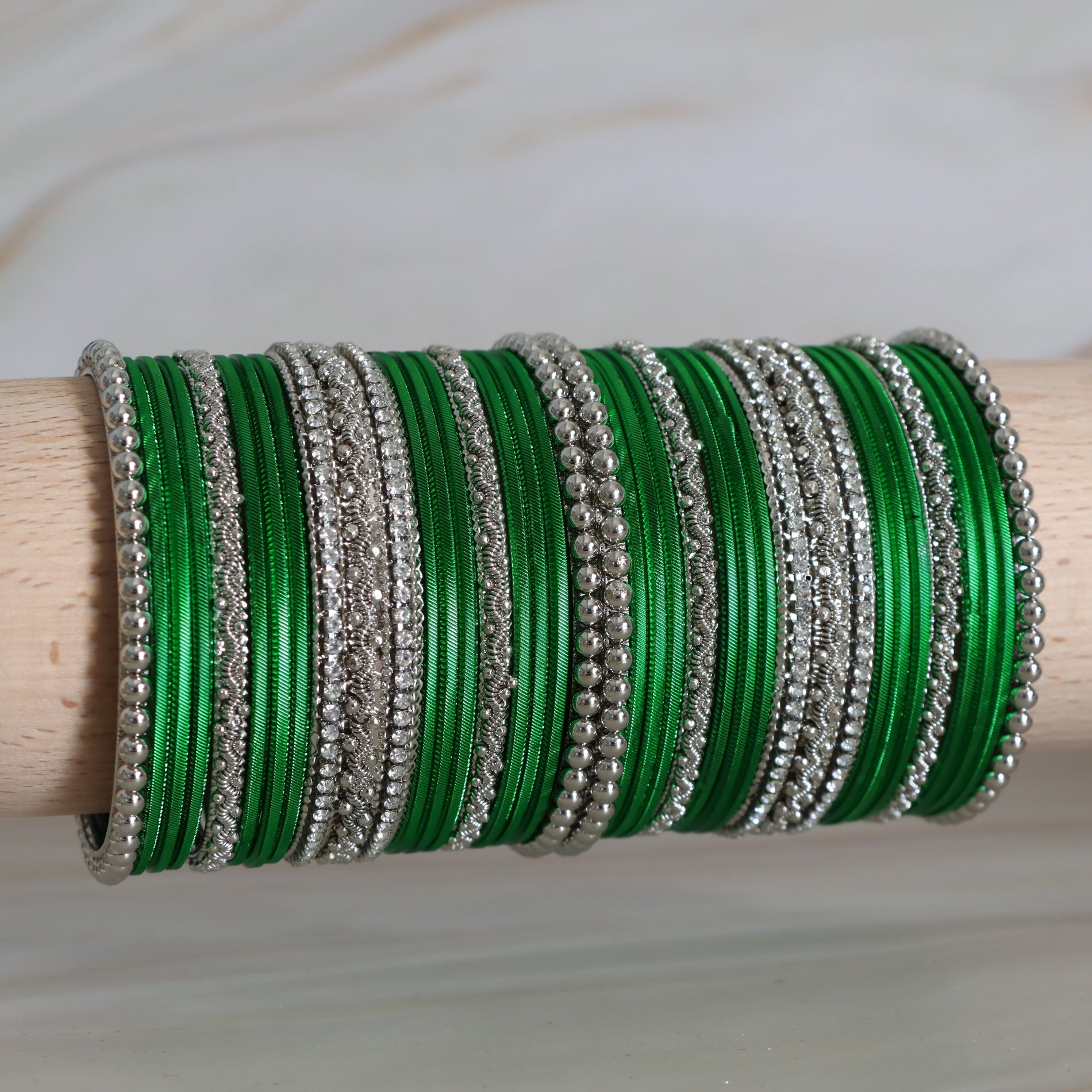 Green and silver bangles stacked on a wooden rod against a neutral background