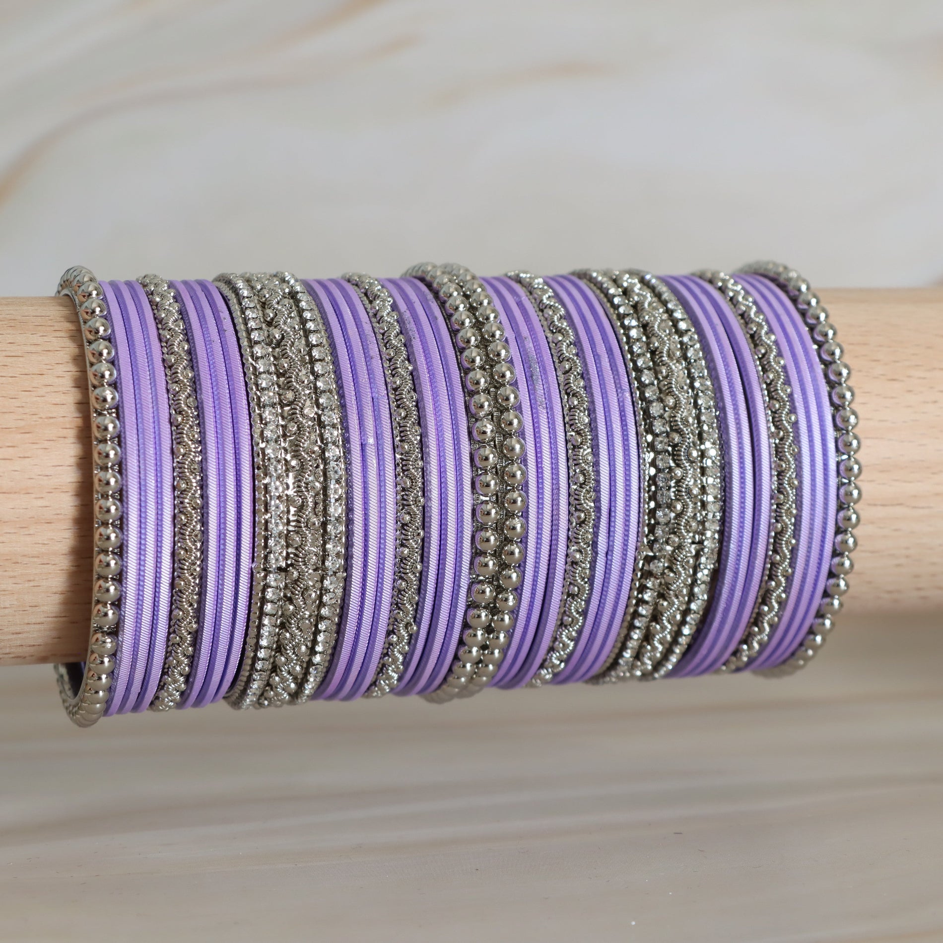 Purple and silver bangles stacked on a wooden stick against a neutral background