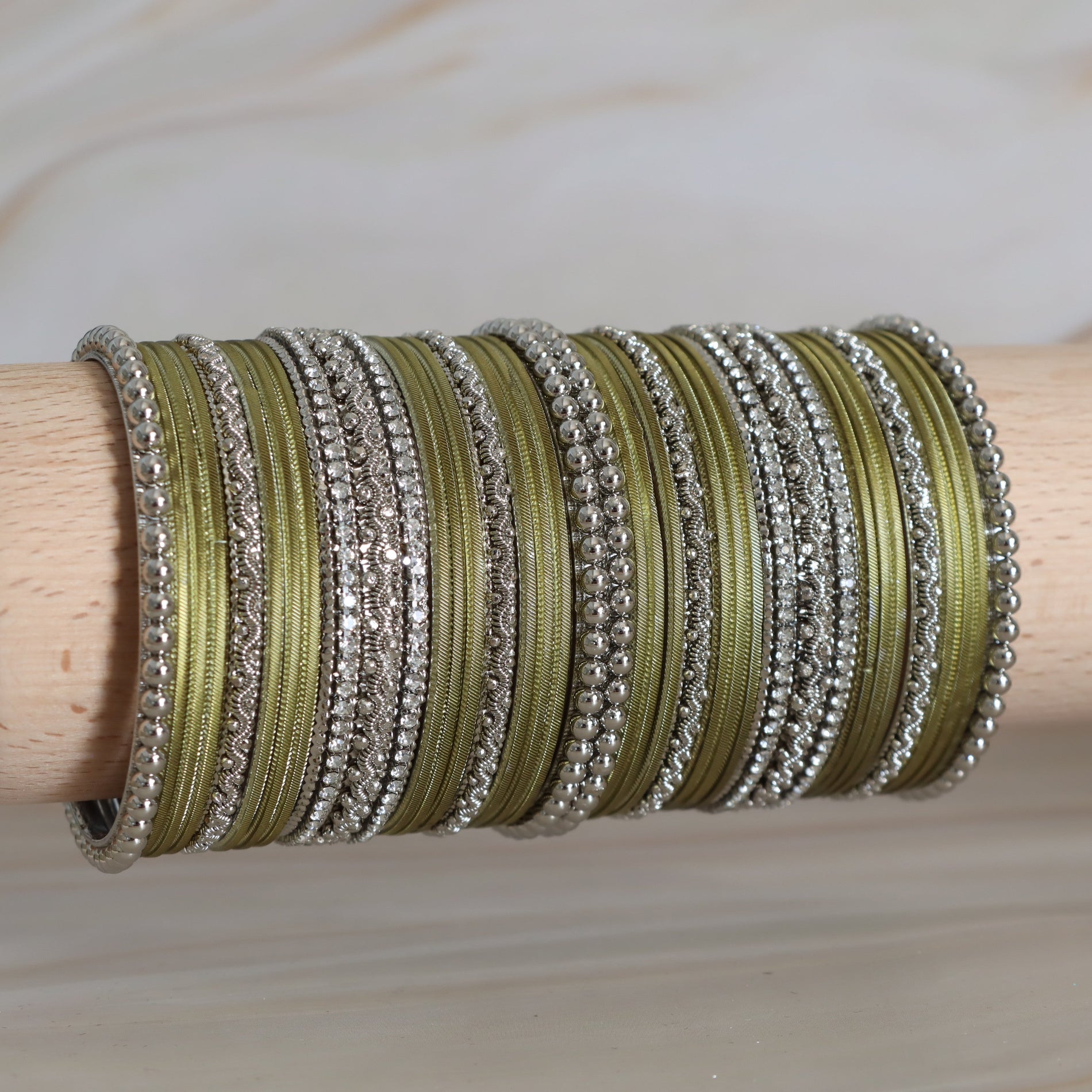 Multiple green and silver bangles stacked on a wooden stick against a neutral background