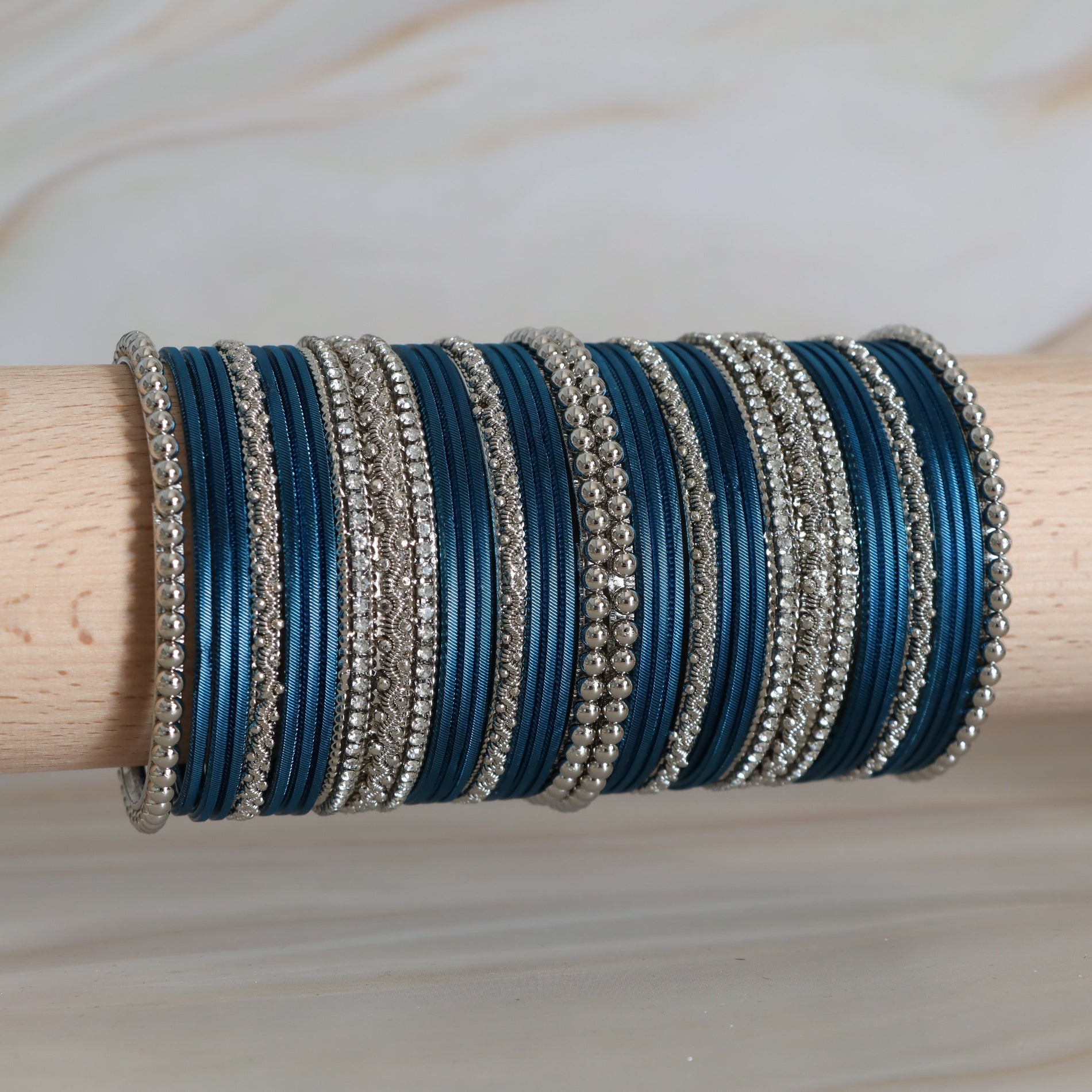 Stack of blue and silver bangles on a wooden stick with a light wood background