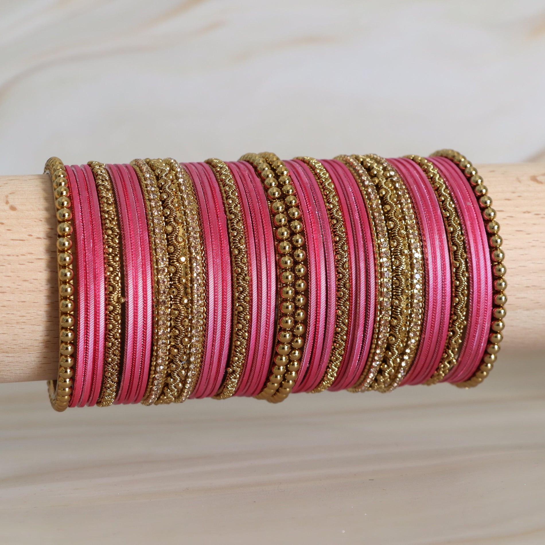Pink and gold bangles stacked on a wooden stick against a neutral background