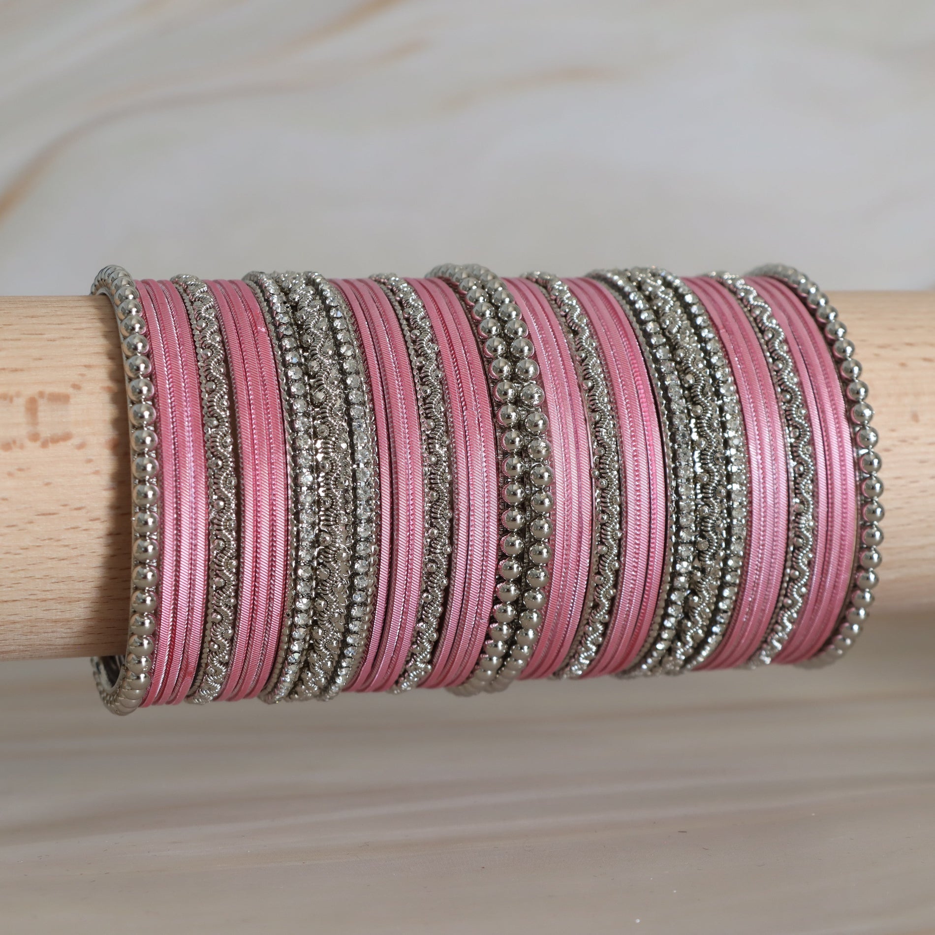 Stack of pink bangles with silver on a wooden stick against a neutral background