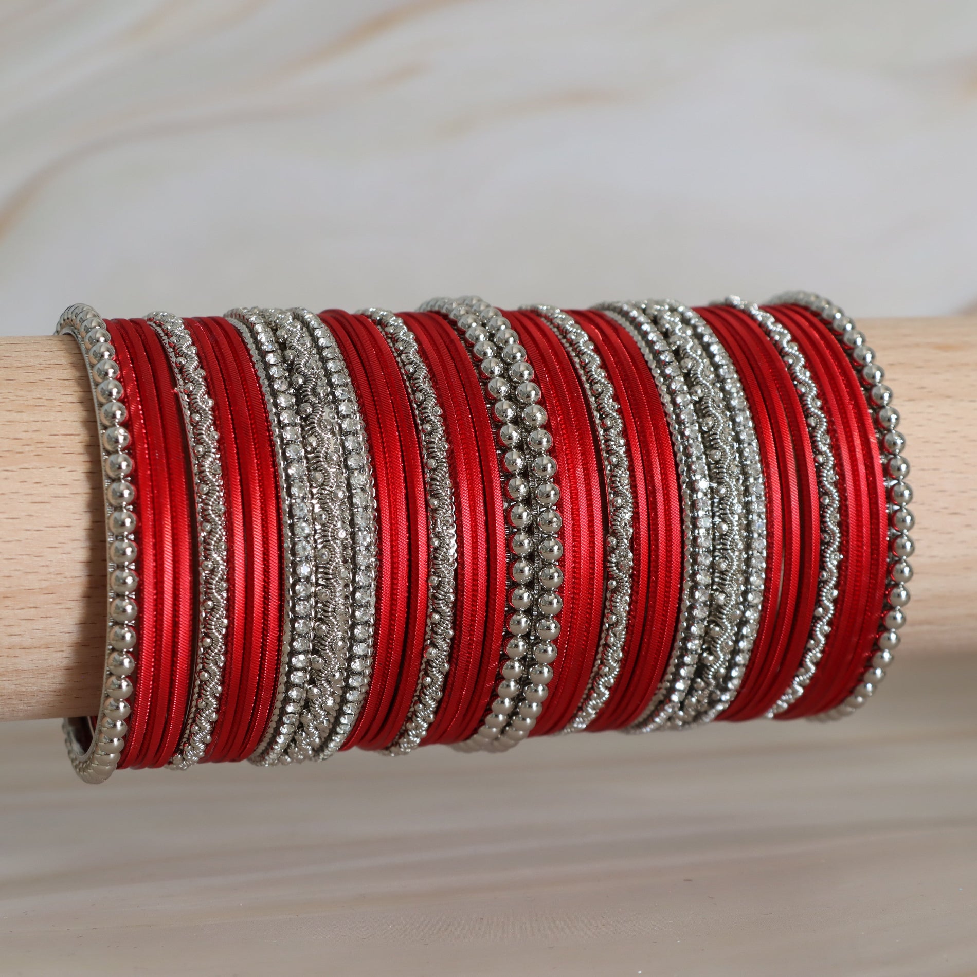 Stack of red and silver bangles on a wooden stick against a neutral background