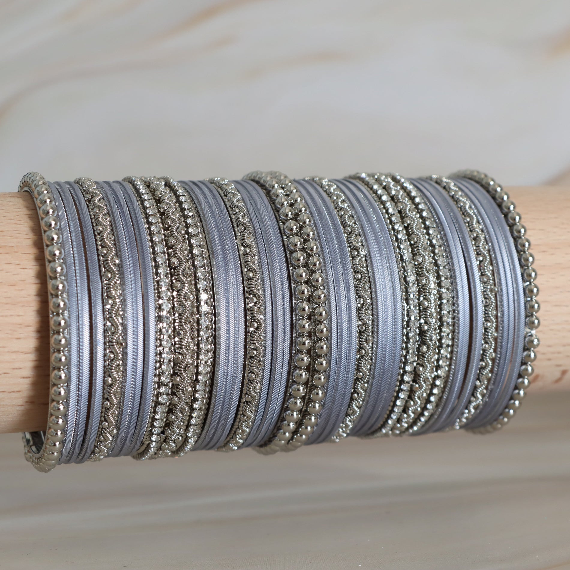Collection of silver and gray bangles on a wooden stick against a neutral background